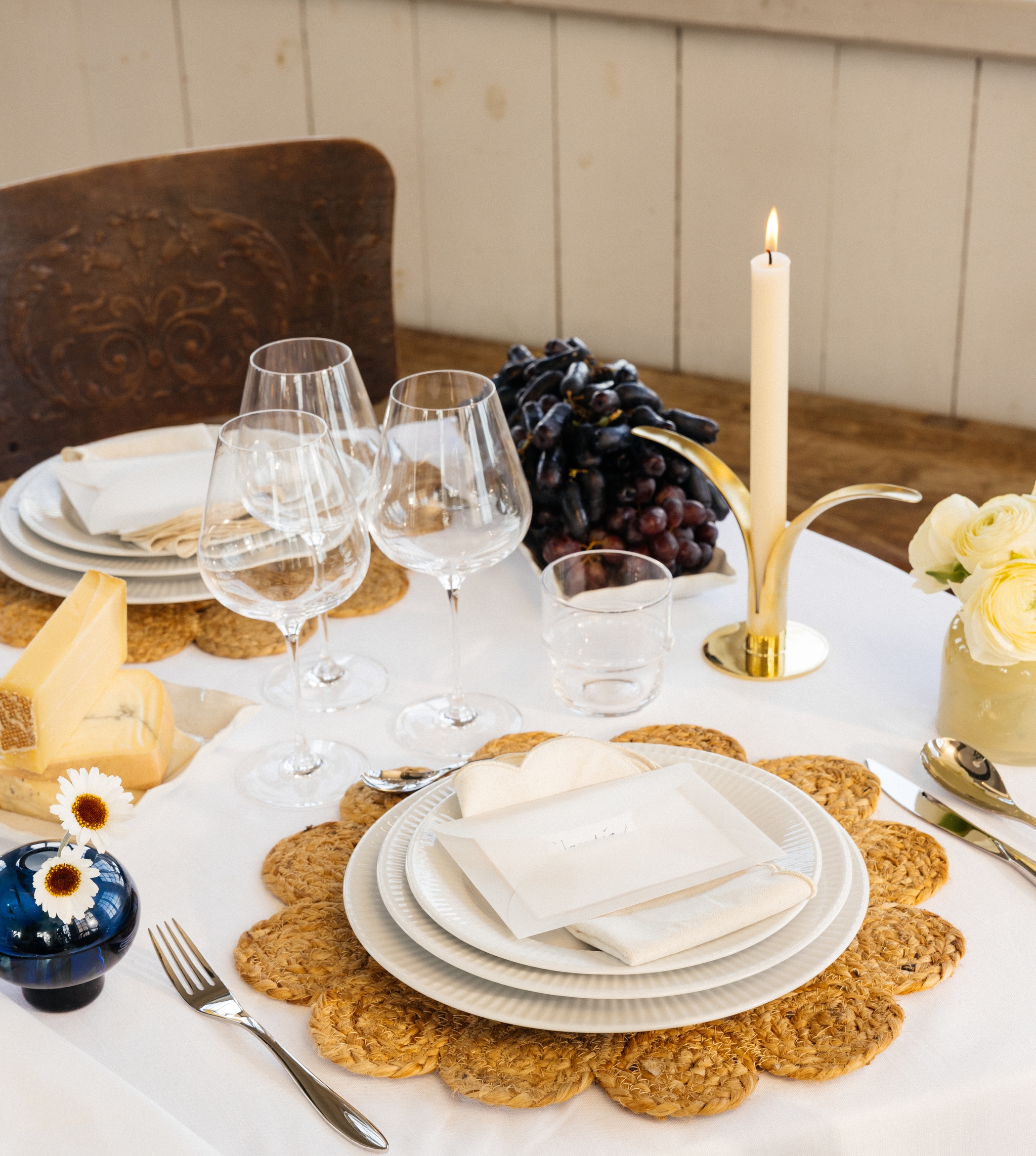 Festdukning med vit duk, bordstabletter, vitt porslin samt gula och blå vaser med blommor i