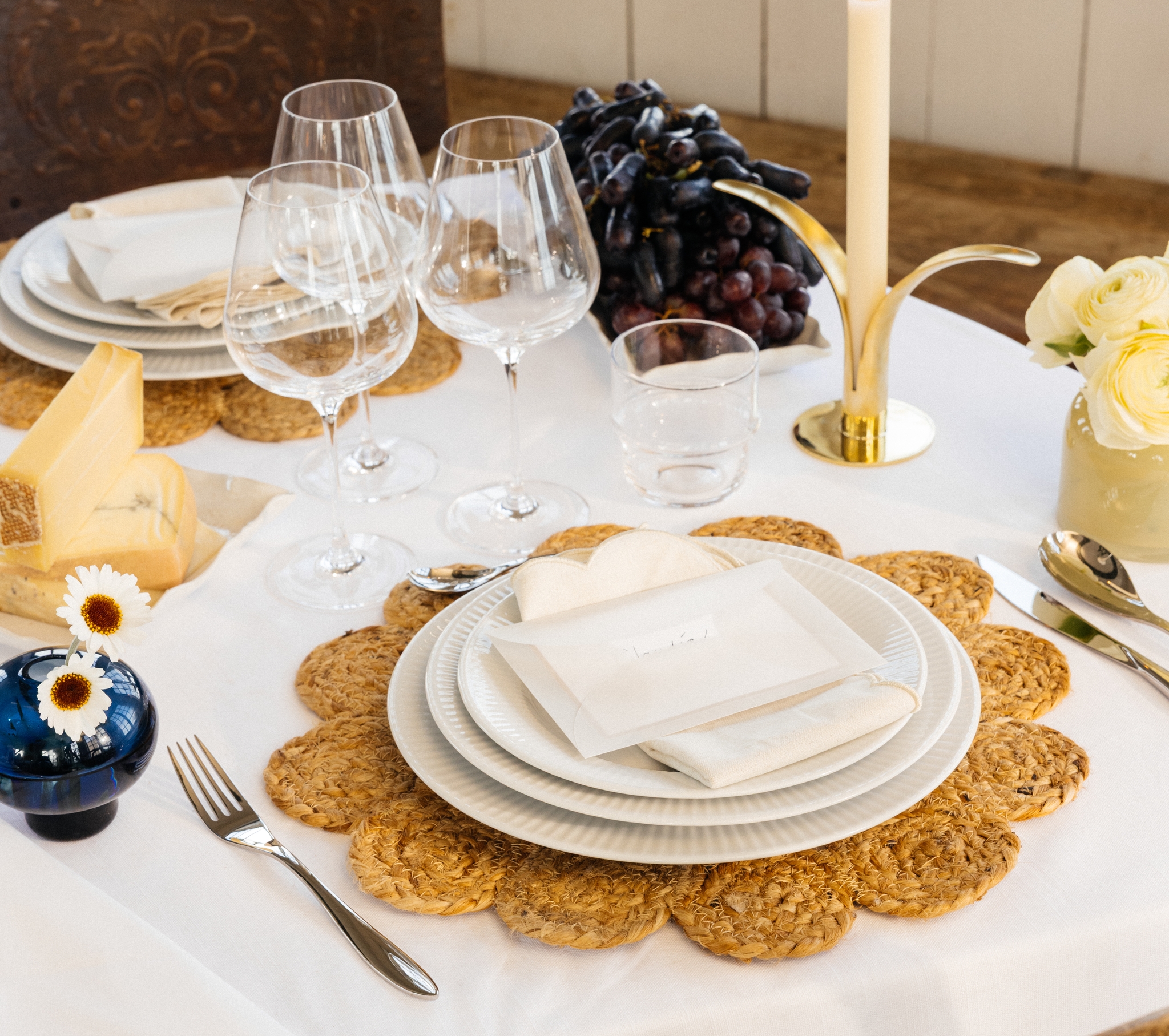 Festlig borddekking med hvit duk, dekkebrikker, hvitt porselen og gule og blå vaser med blomster i
