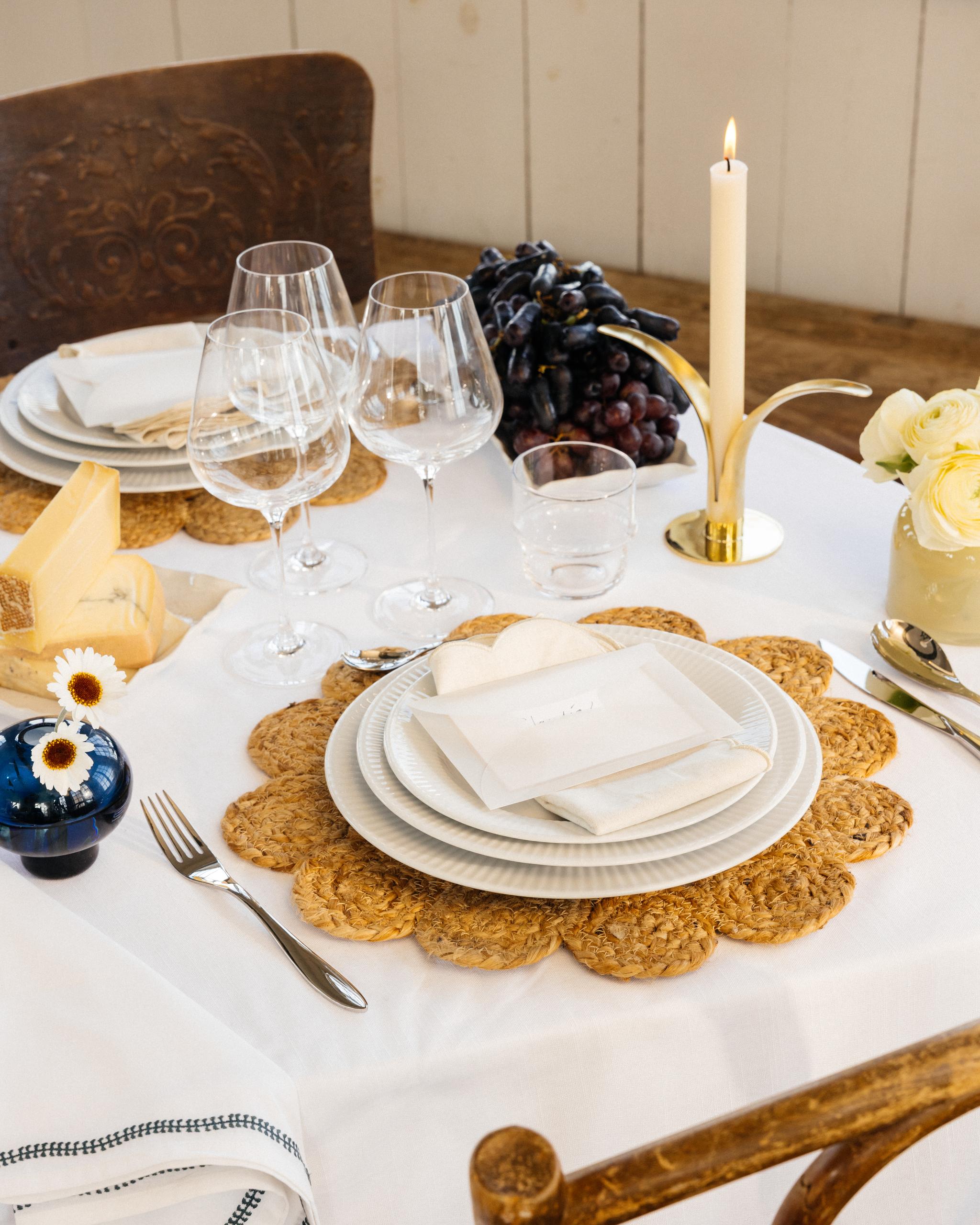 Juhlallinen kattaus, jossa valkoinen pöytäliina, pöytämatot, valkoinen posliini ja keltaiset ja siniset kukkamaljakot
