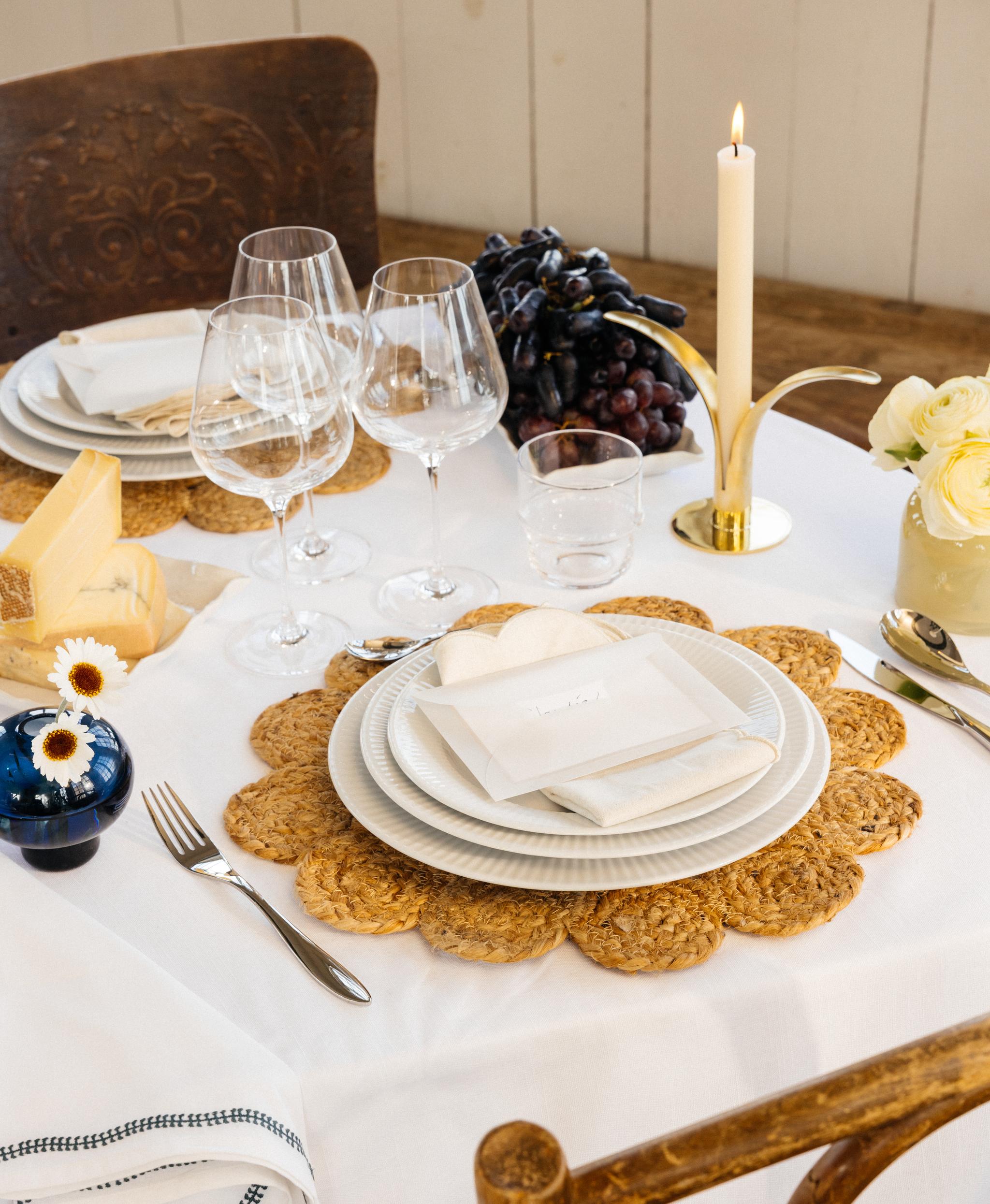 Festlig borddekking med hvit duk, dekkebrikker, hvitt porselen og gule og blå vaser med blomster i