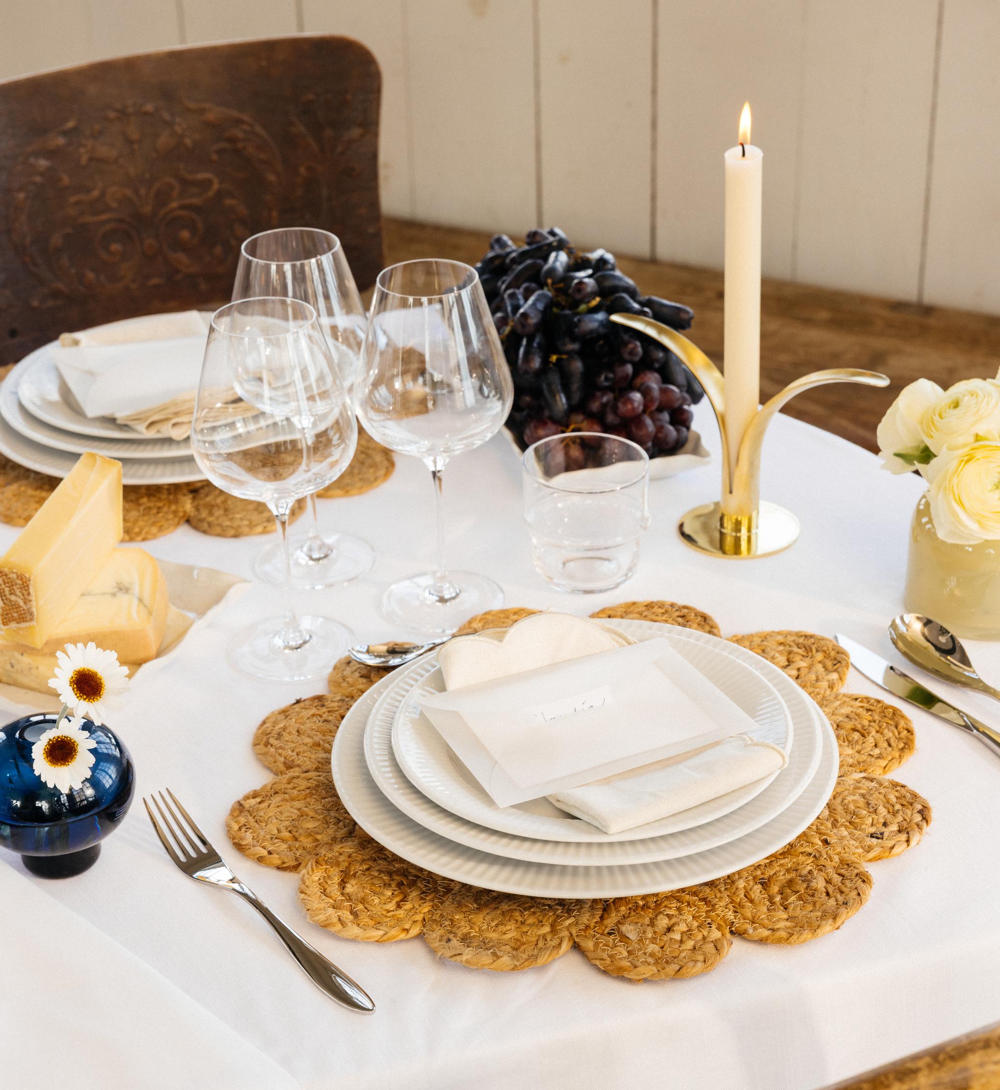 Festdukning med vit duk, bordstabletter, vitt porslin samt gula och blå vaser med blommor i