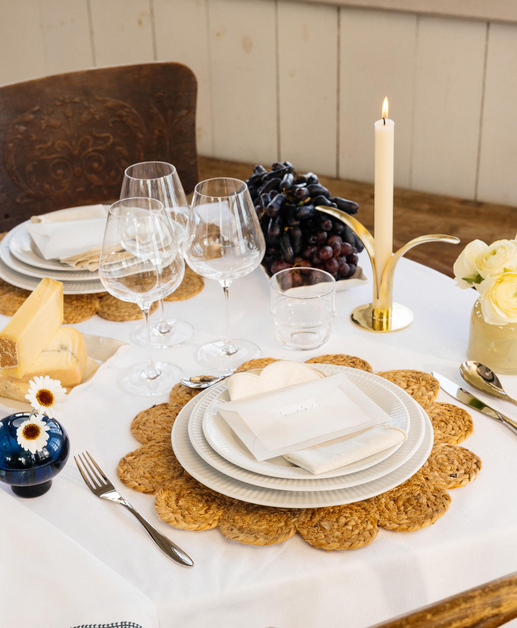Festlig borddekking med hvit duk, dekkebrikker, hvitt porselen og gule og blå vaser med blomster i
