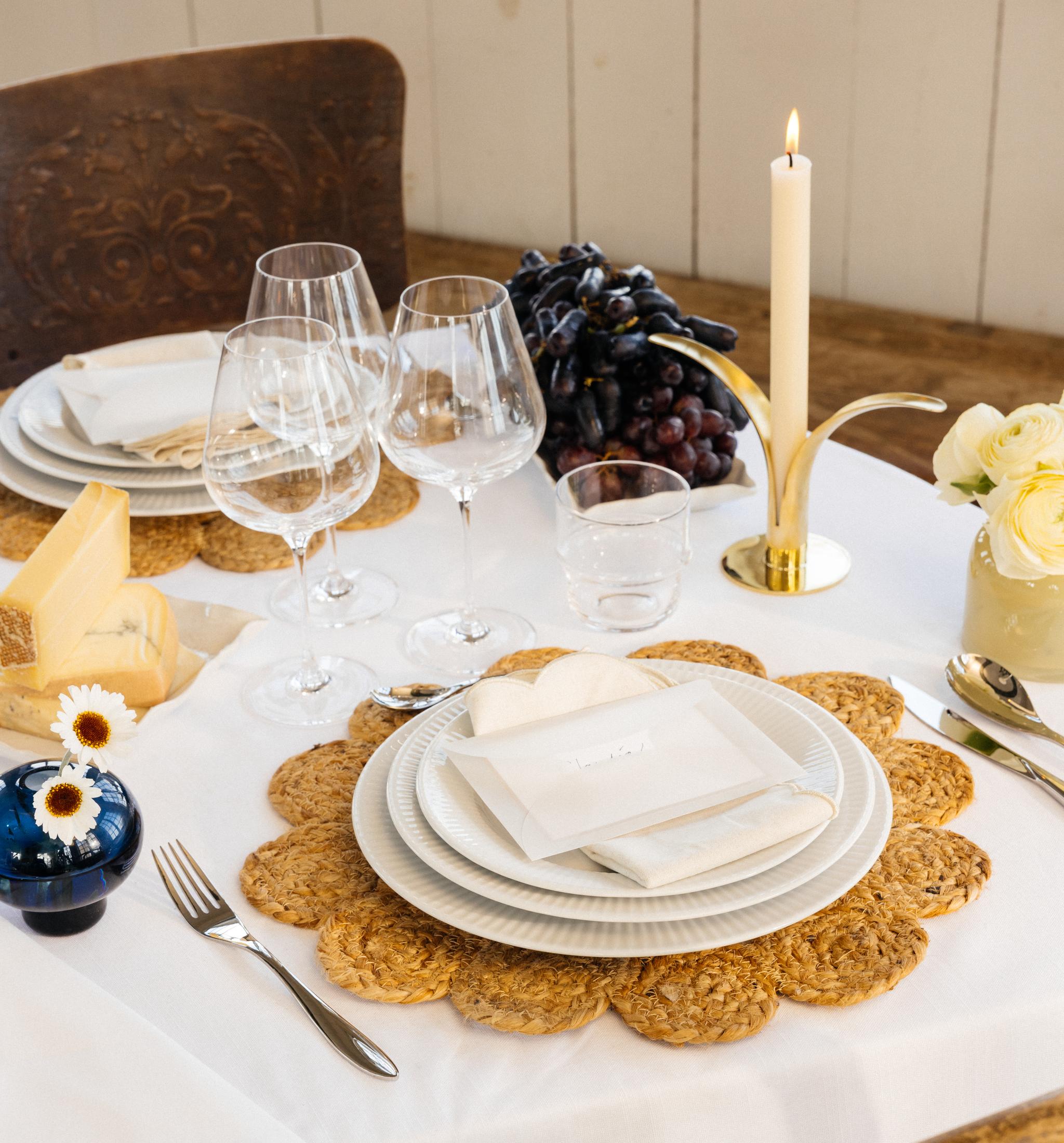 Festdukning med vit duk, bordstabletter, vitt porslin samt gula och blå vaser med blommor i