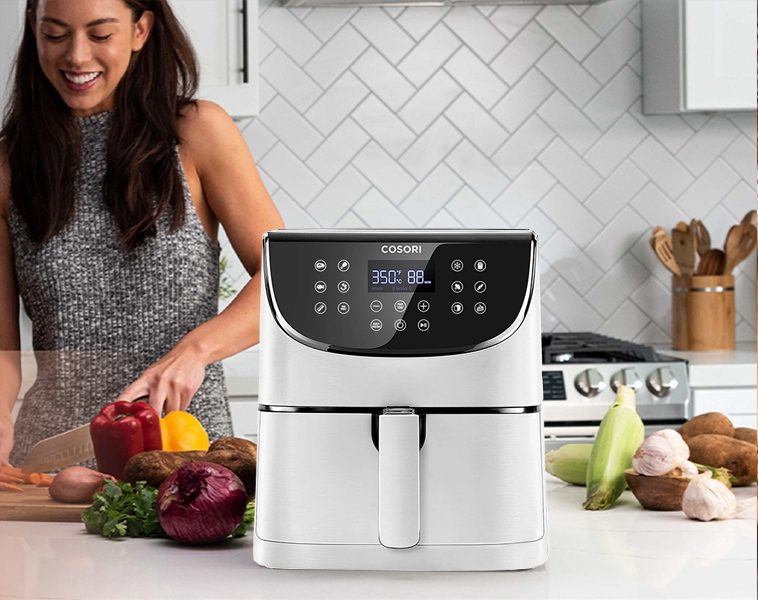 Valkoinen airfryer keittiössä ja nainen ketä pilkkoo vihanneksia