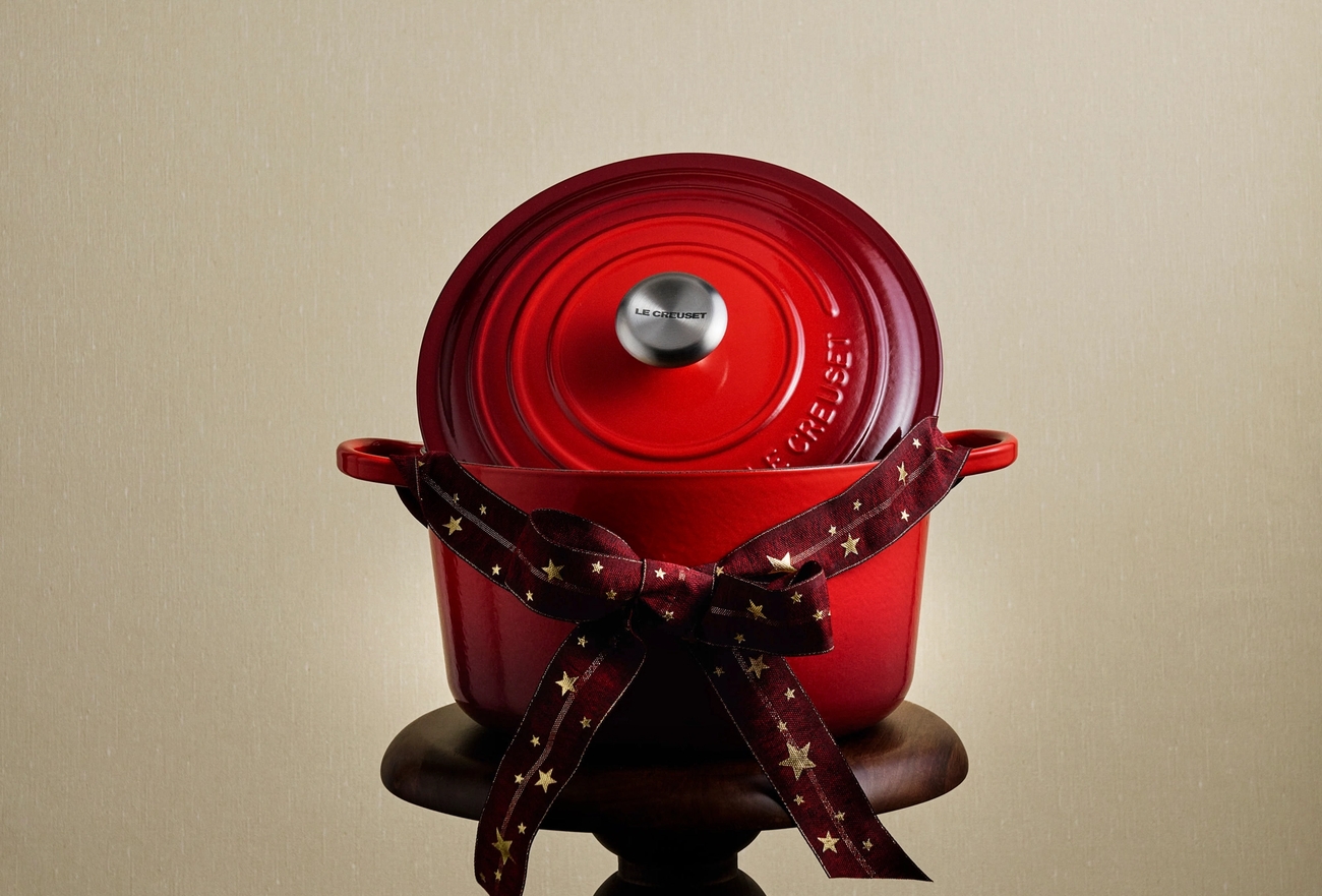 Punainen Le Creuset -ruukku, joka on sidottu tähtikuvioisella nauhalla, on puisella jalustalla.