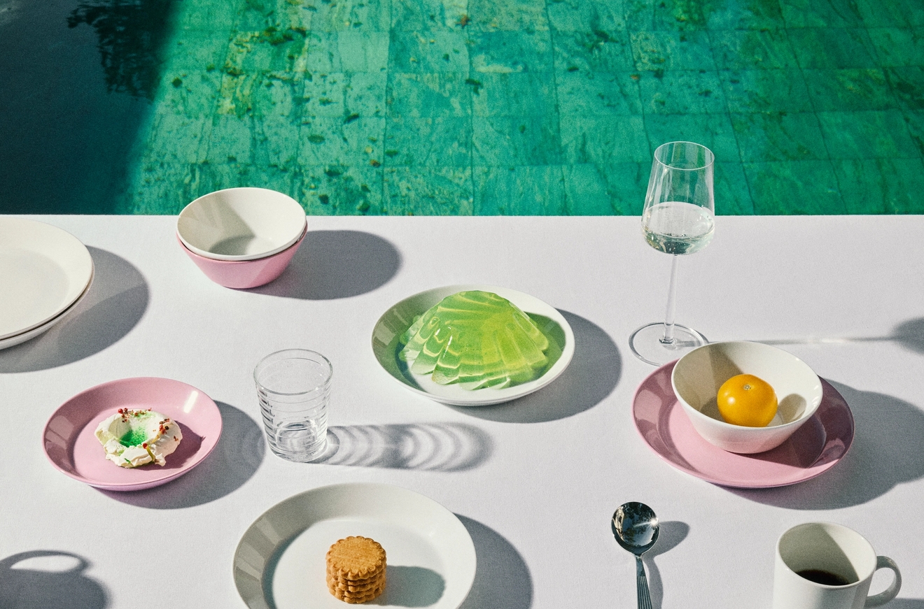 Ett vitt bord med en uppsättning rosa och vita fat med små snacks och drycker, intill en turkos pool.