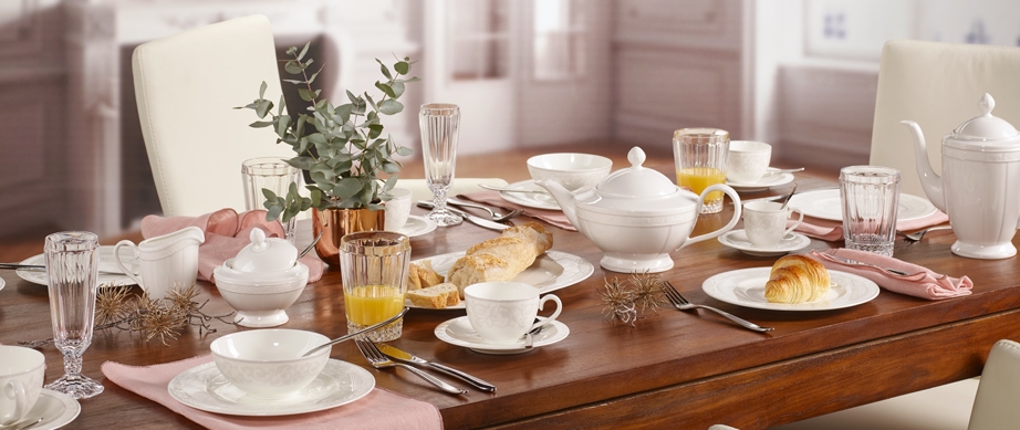 Elegant dukat frukostbord med vitt porslin, croissanter, juice och blommor i en ljus matsal.