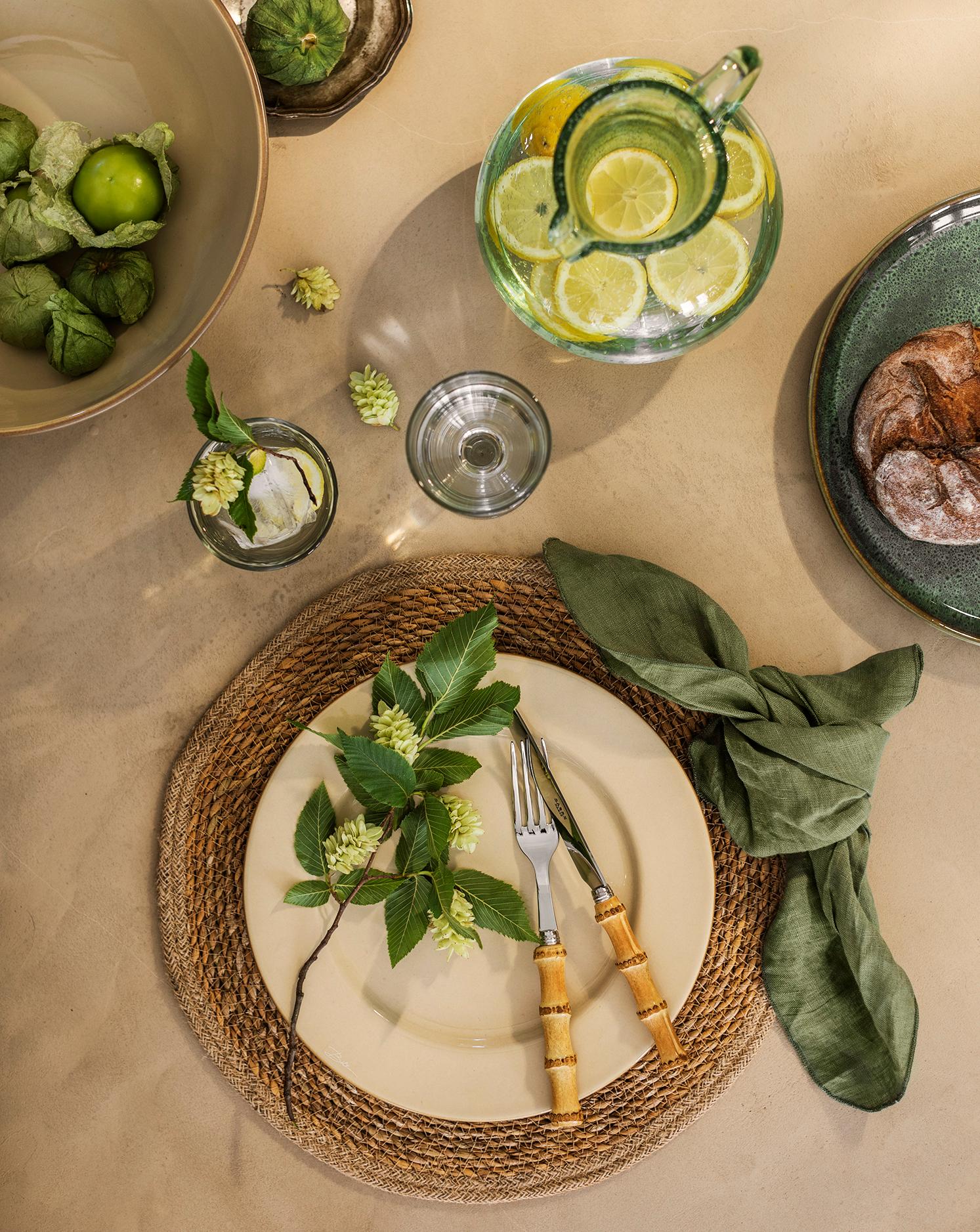 Festlig borddekking i jordfarger med beige tallerken og grønn serviett på jute dekke