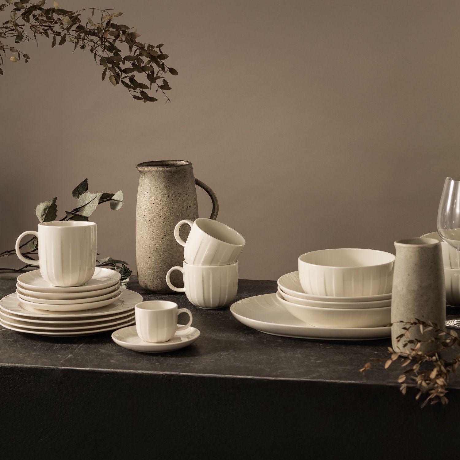 Elegant dukning med vitt porslin, keramikkannor och dekorativa kvistar på ett mörkt bord.