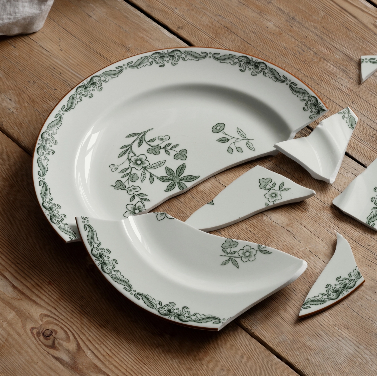 En trasig Ostindia Grön mattallrik som ligger på ett trägolv