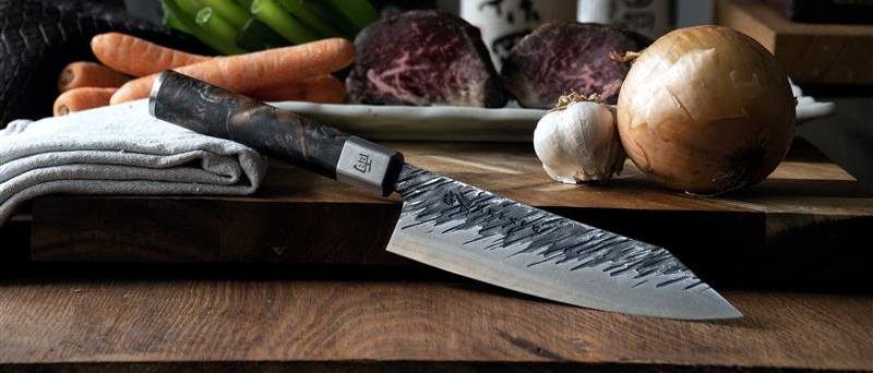 Satake kniver på et skjærebrett med skivet agurk, purreløk og en blå duk