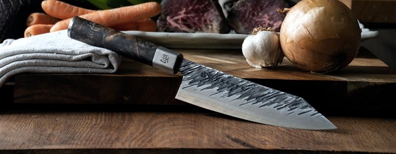 Satake knivar på en skärbräda med skivad gurka, purjolök och en blå bordsduk