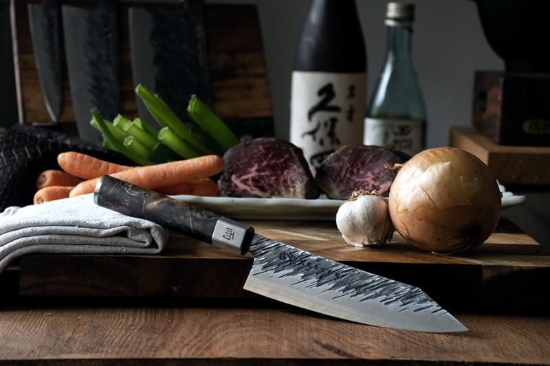 Satake kniver på et skjærebrett med skivet agurk, purreløk og en blå duk