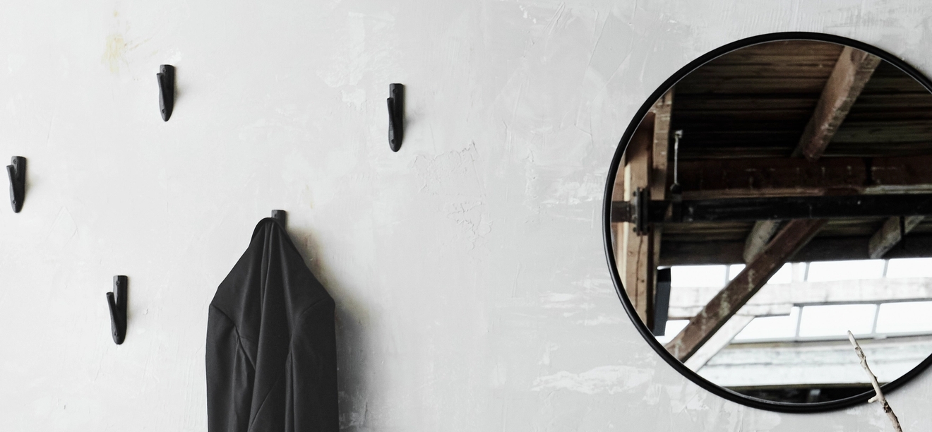 mustat koukut ja pyöreä peili harmaalla seinällä