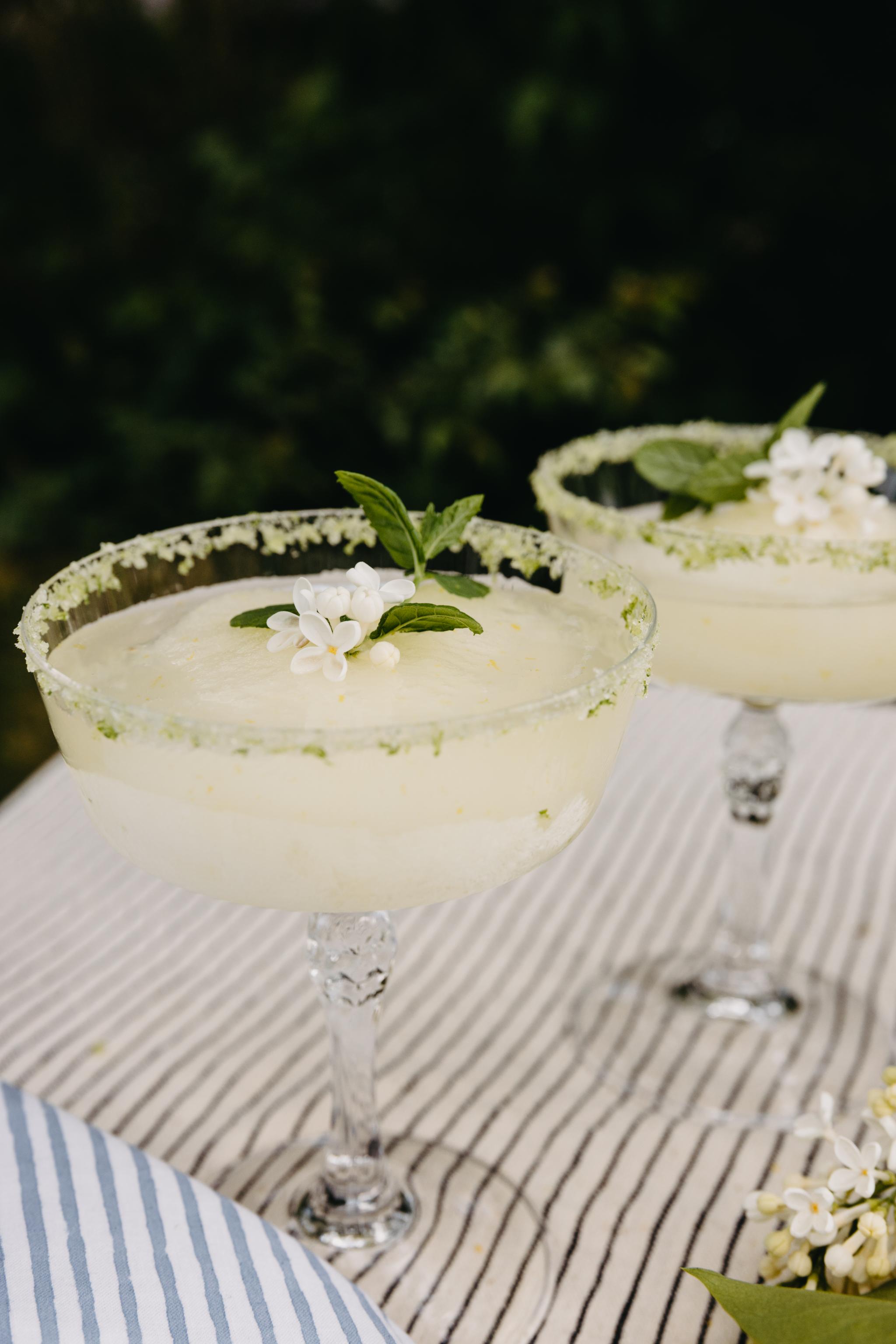 Kellertävä drinkki cocktaillasissa raidallisella pöytäliinalla