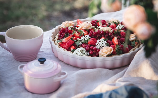 Vaaleanpunainen Le creuset piirakkavuoka, annosvuoka ja muki pöydällä