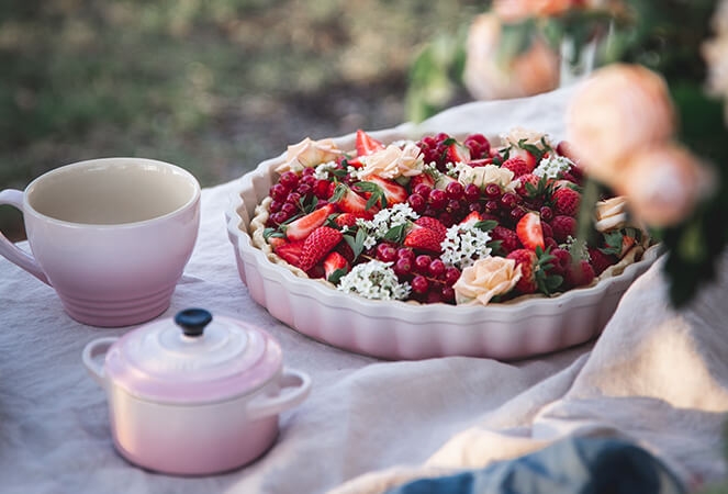 Vaaleanpunainen Le creuset piirakkavuoka, annosvuoka ja muki pöydällä