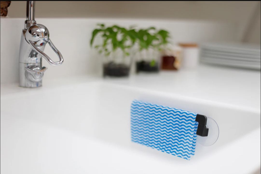 A blue wavy dishcloth is held by a suction cup holder inside a white kitchen sink with a chrome faucet.