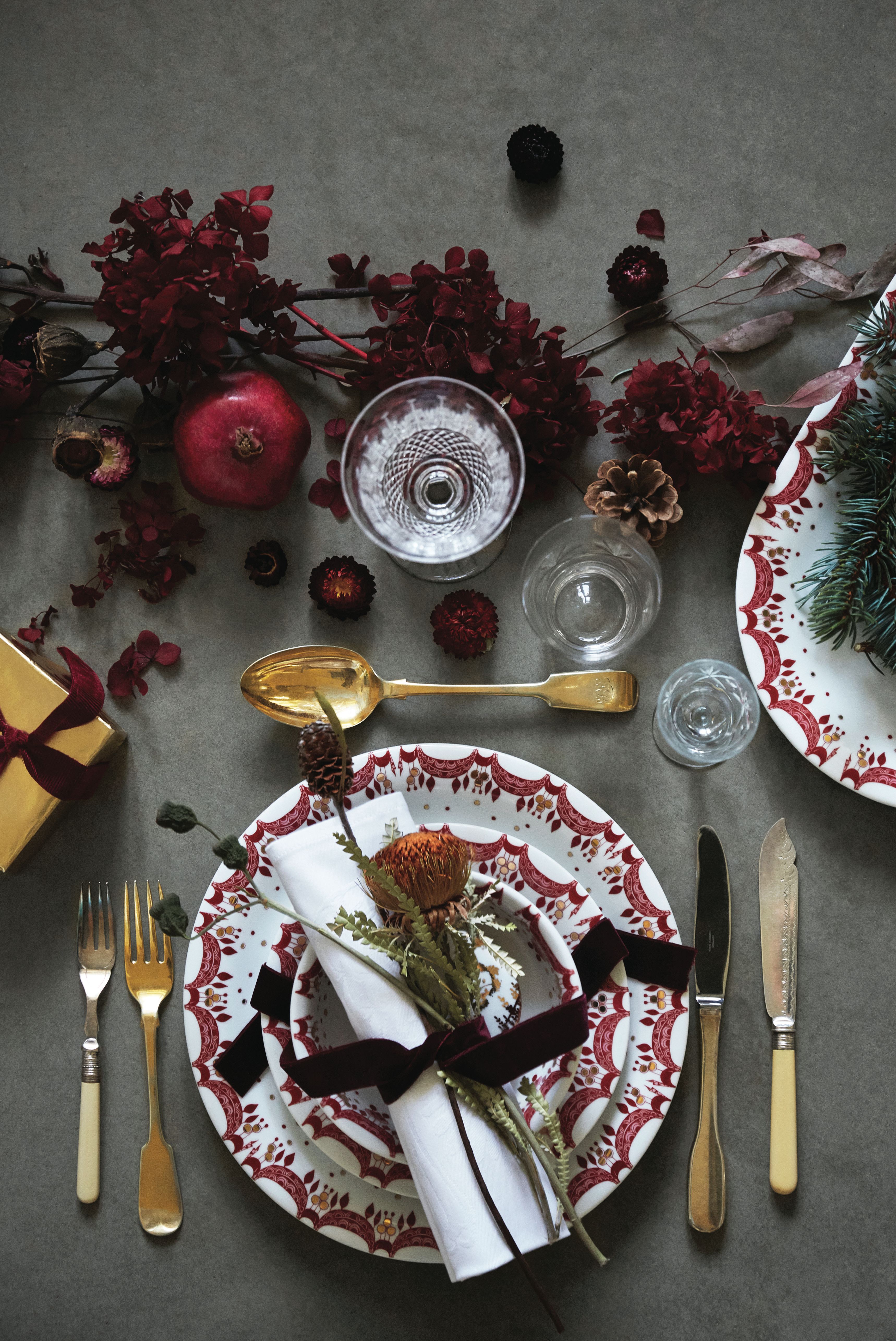 Juleborddekking med gullbestikk og hvite tallerkener med en rød julegirlander