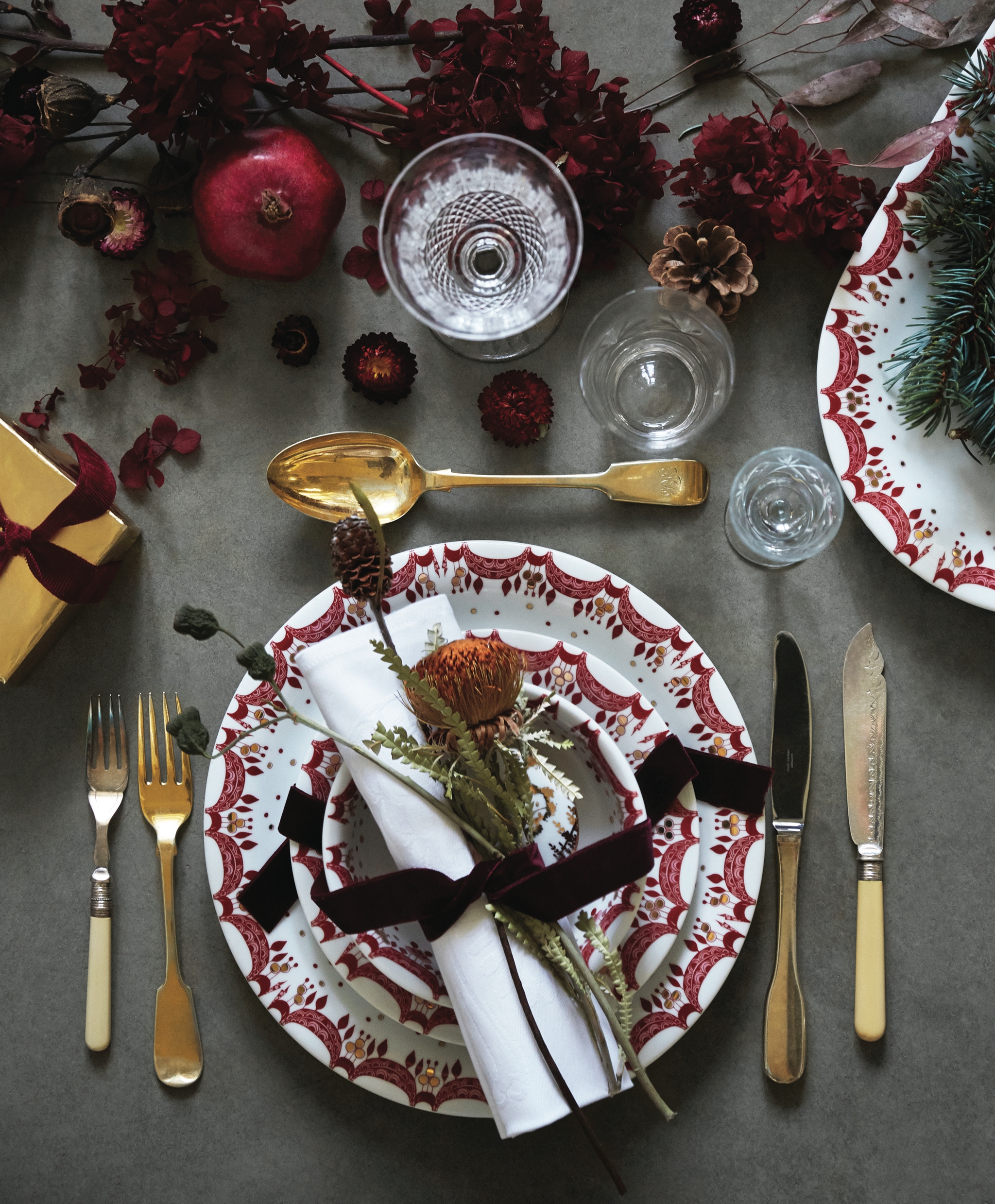 Juleborddekking med gullbestikk og hvite tallerkener med en rød julegirlander