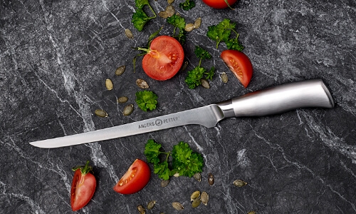 Tomatkniv med oppdelte tomater på en svart marmorplate