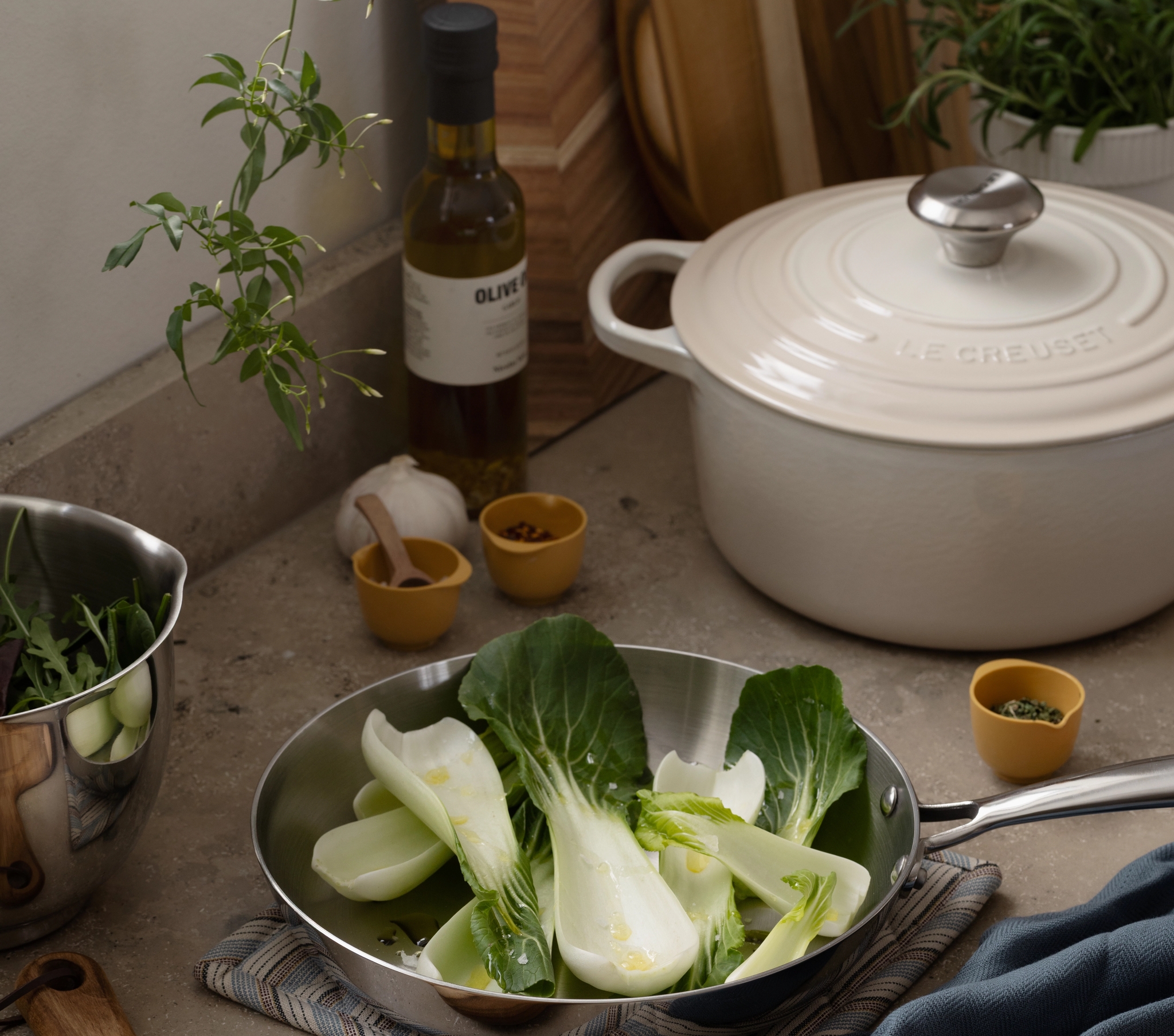 Bok choy in a pan on a kitchen counter with a cutting board, knife, and small bowls.