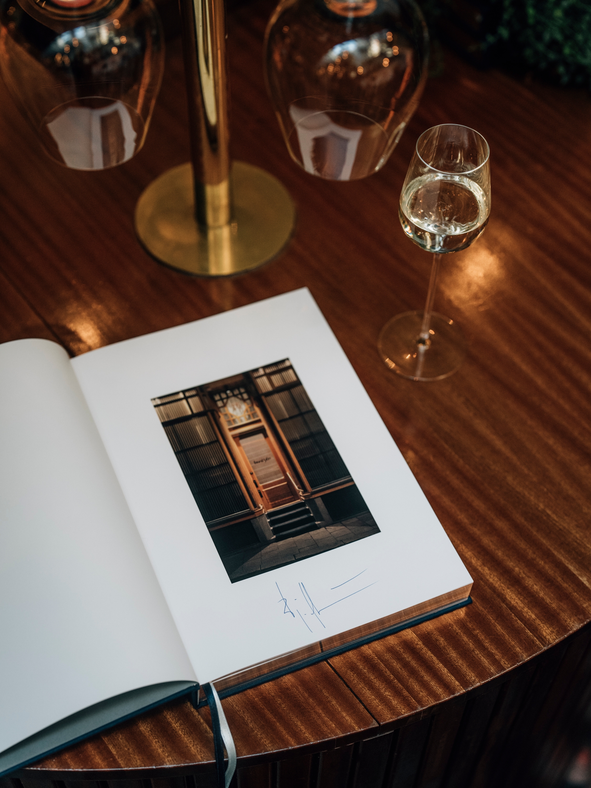 En uppslagen coffeetable bok som ligger på ett träbord med ett glas vin bredvid