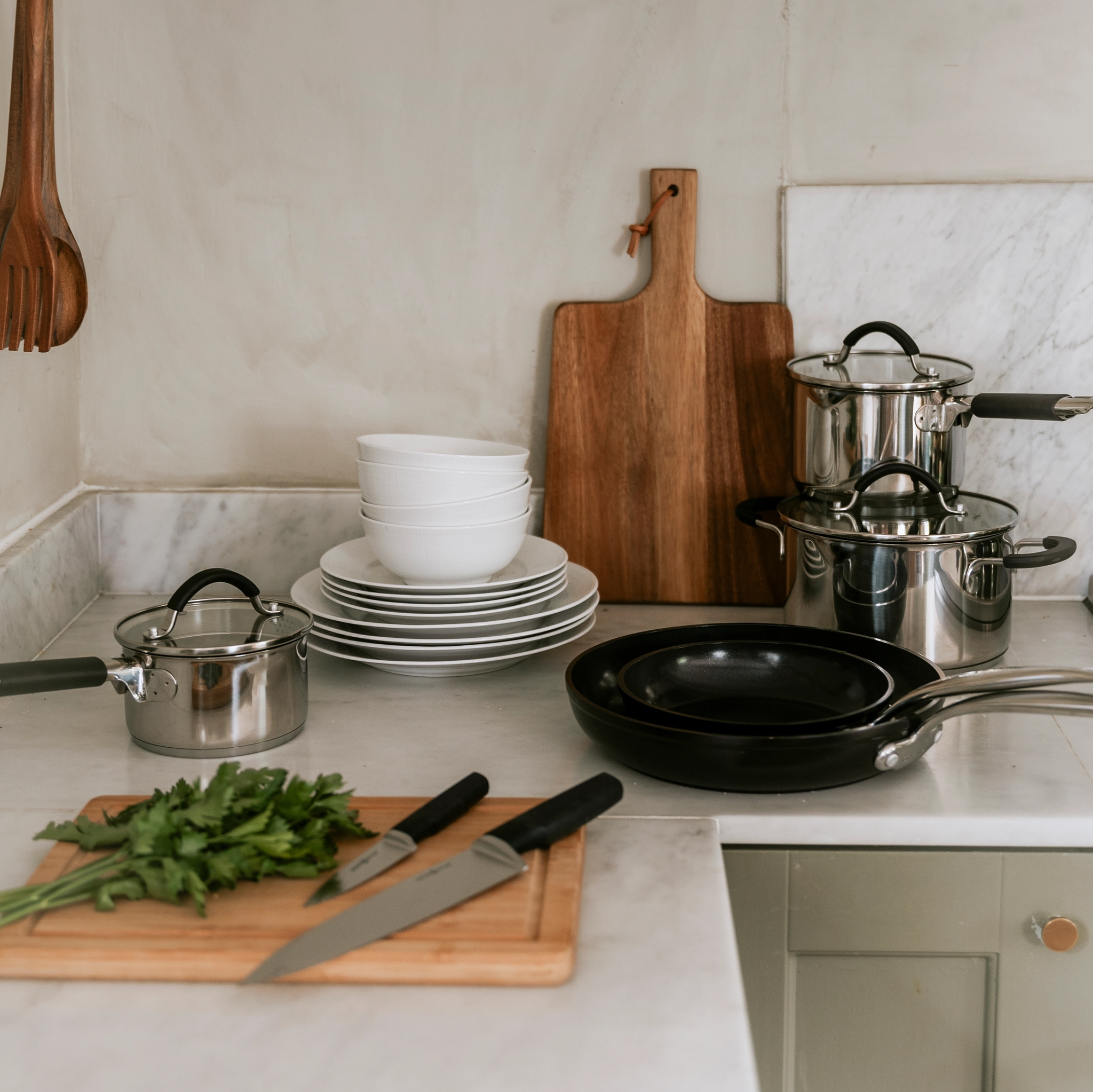 Kitchen counter with pots, pans, stacked dishes, and a cutting board with parsley and knives.