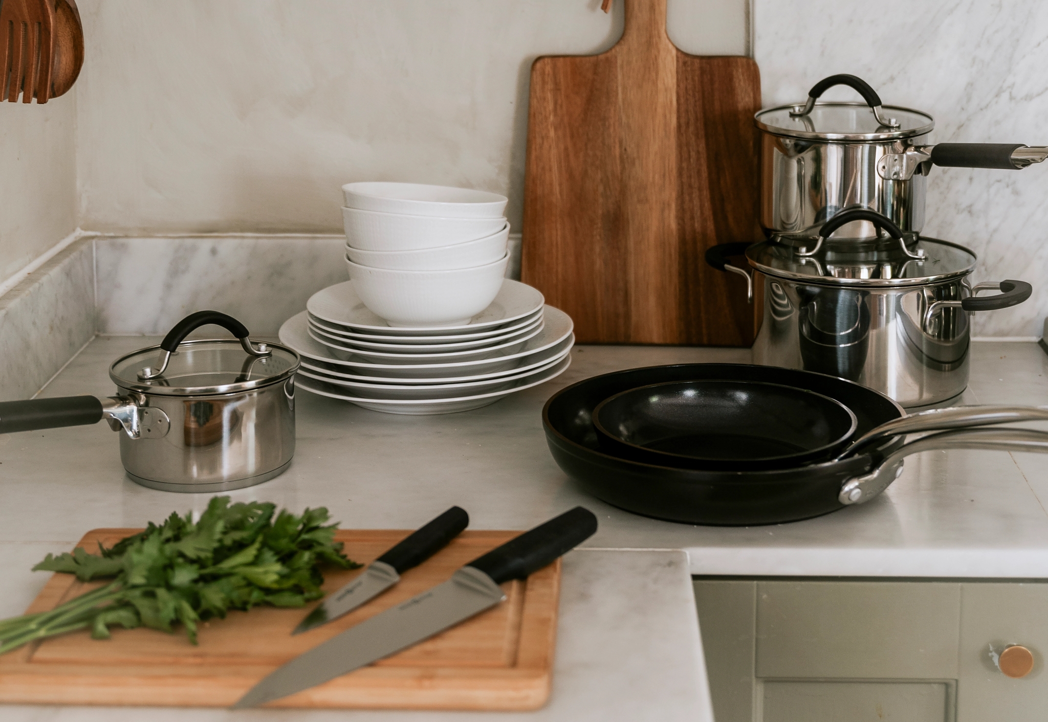 Kitchen counter with pots, pans, stacked dishes, and a cutting board with parsley and knives.