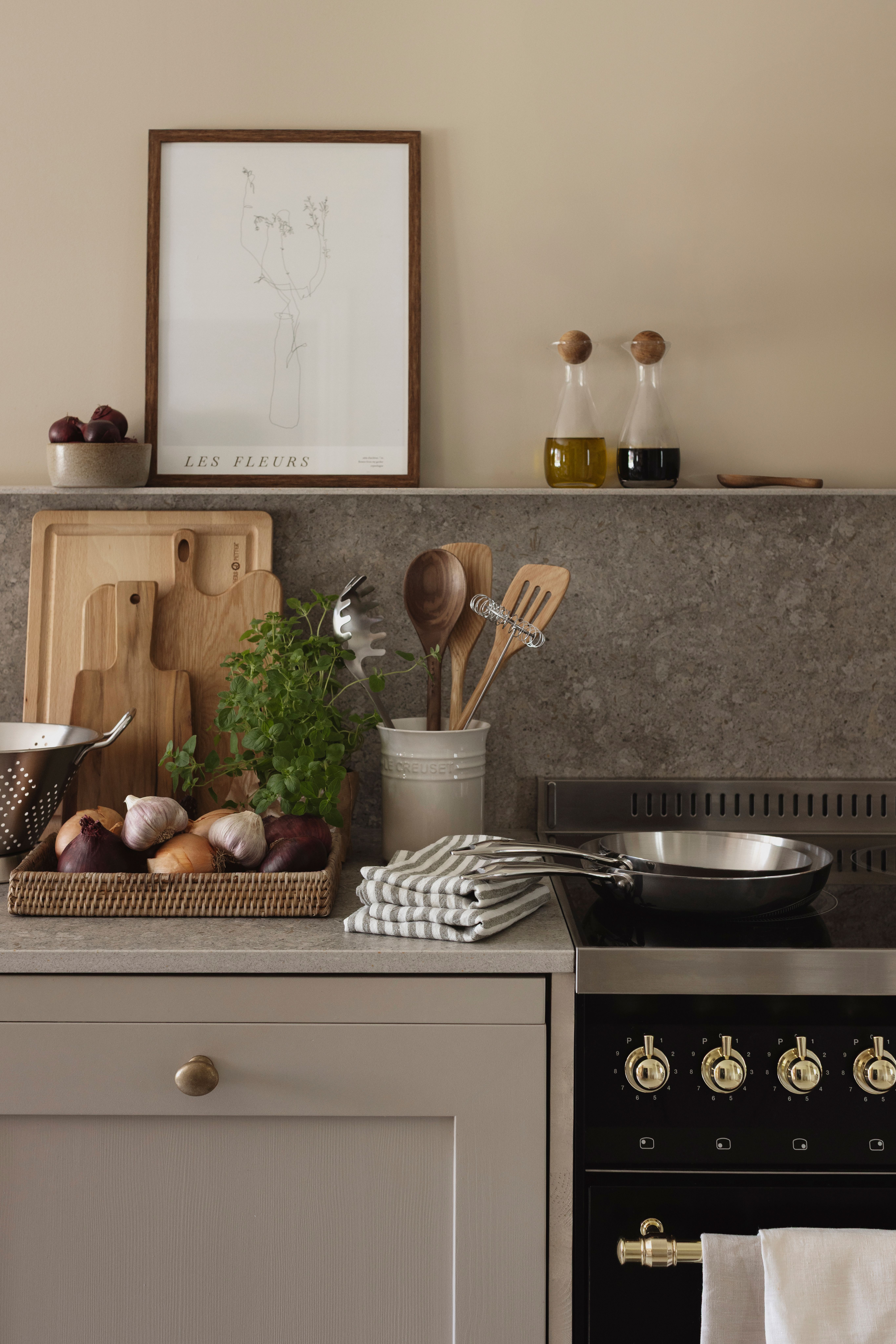 En organiserad modern köksbänk med färska råvaror, skärbrädor, köksredskap, en spishäll och en inramad blommotiv.