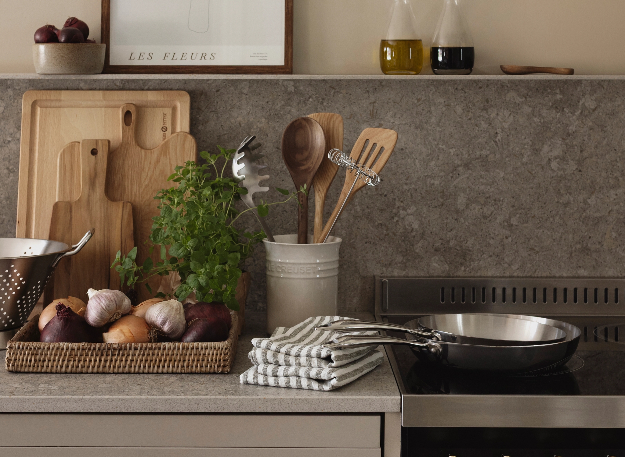 Stilren köksbänk i beige med kryddor, lök, örter, skärbrädor och stekpanna framför en modern spis.