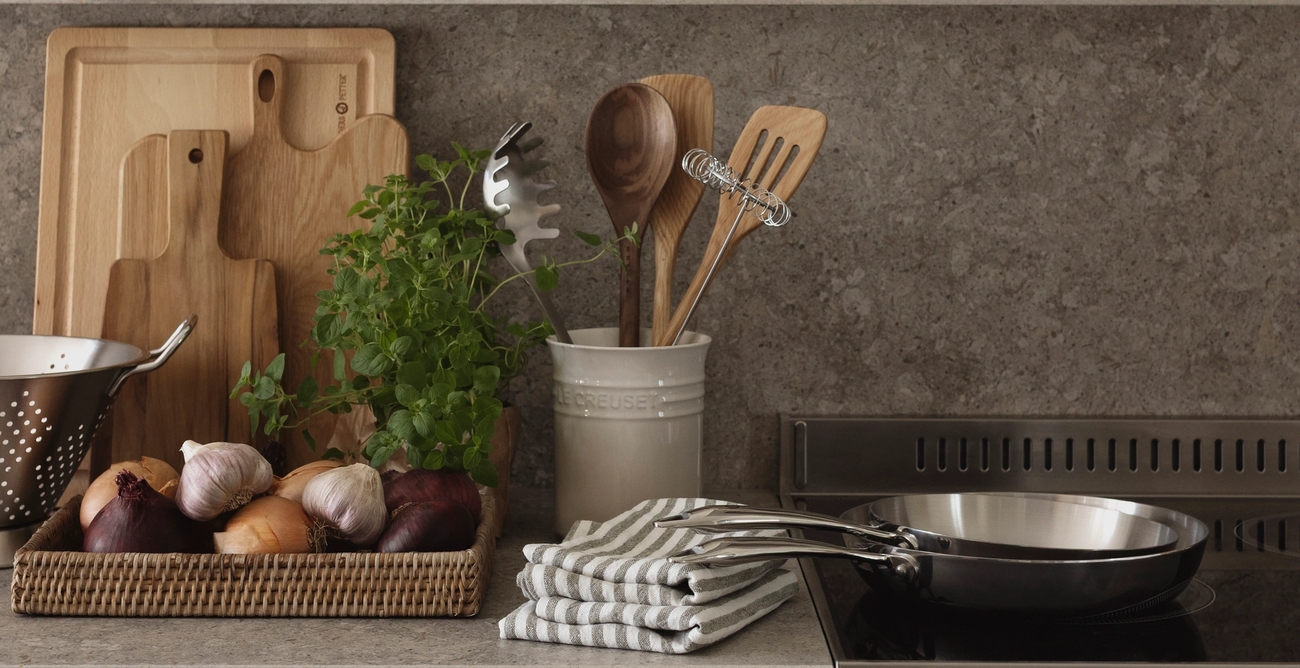 Järjestetty moderni keittiötaso, jossa on tuoreita raaka-aineita, leikkuulautoja, keittiövälineitä, keittotaso ja kehystetty kukkataulu.