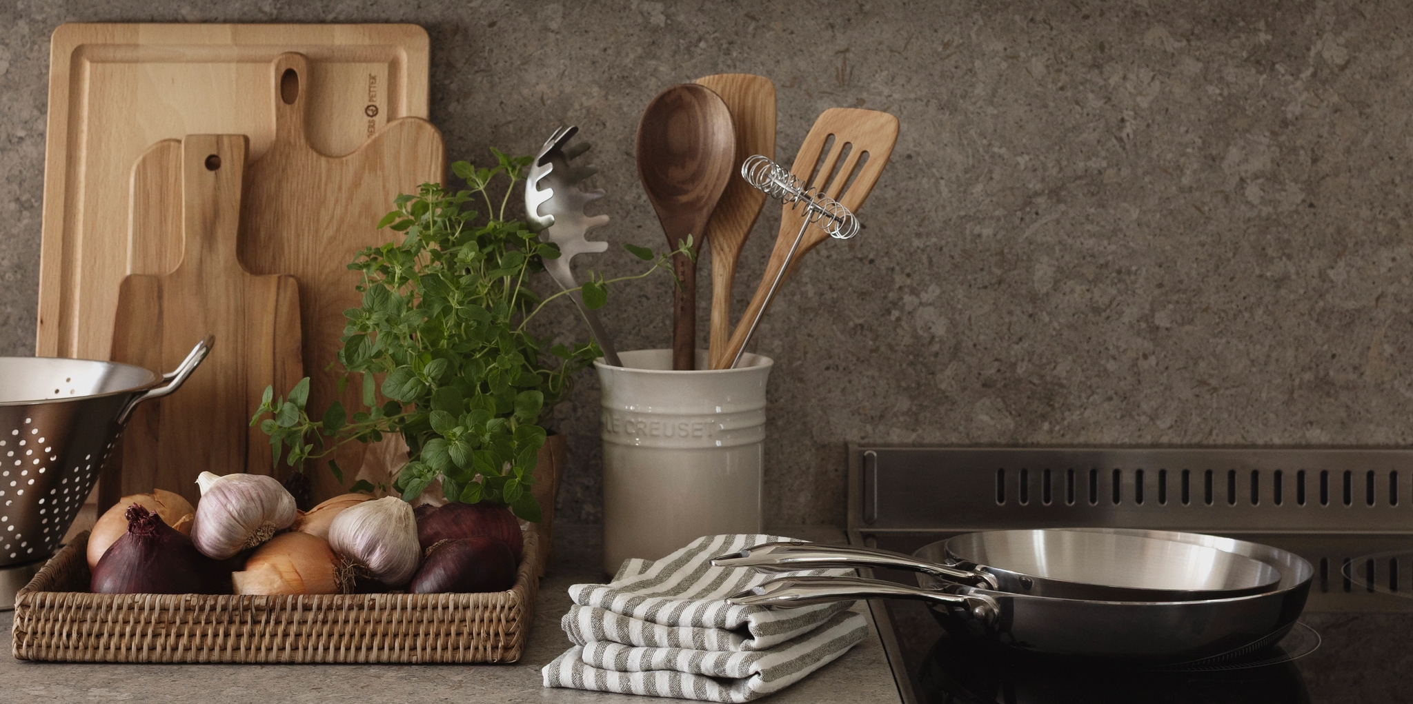 En organiserad modern köksbänk med färska råvaror, skärbrädor, köksredskap, en spishäll och en inramad blommotiv.