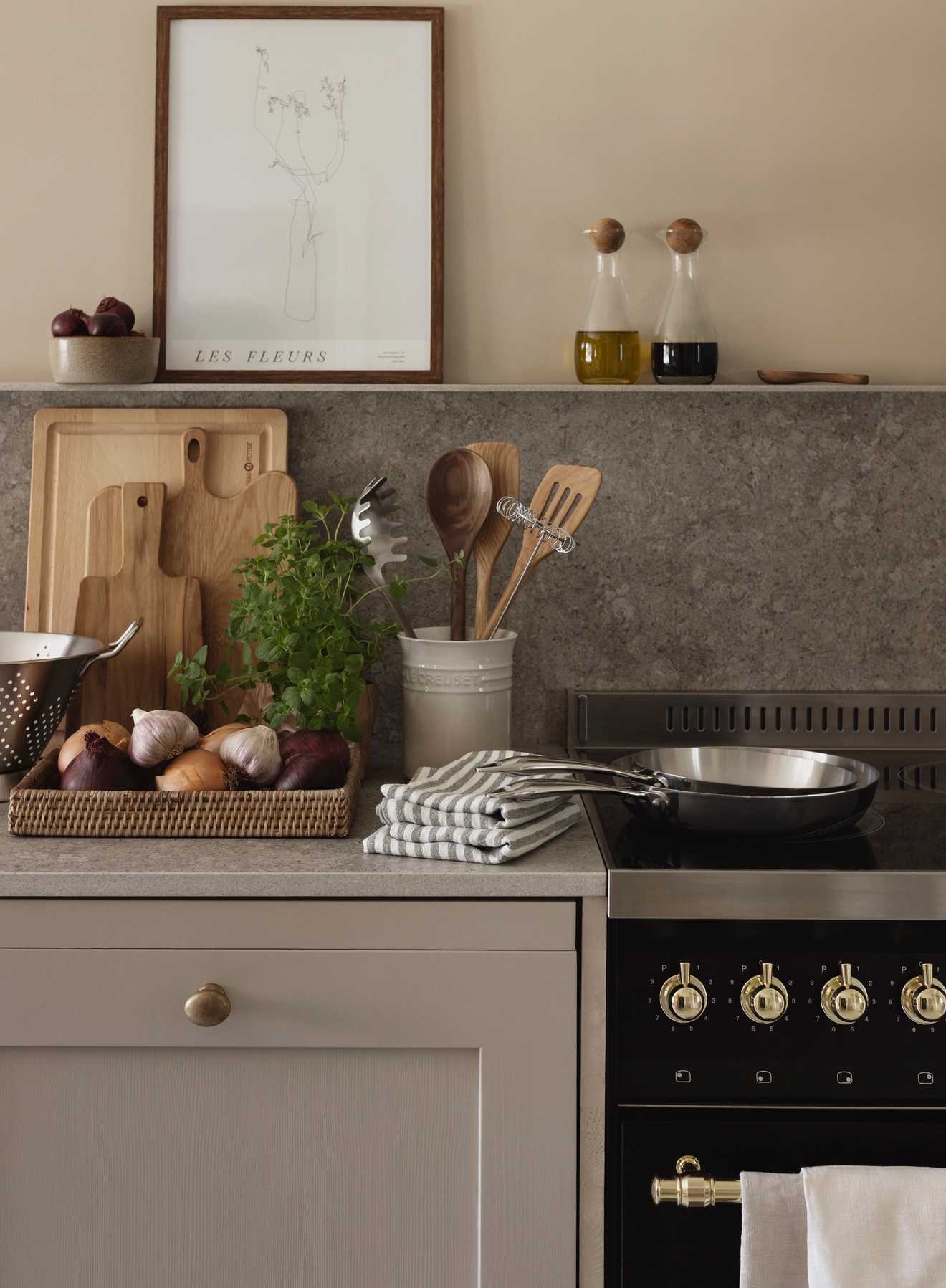 Järjestetty moderni keittiötaso, jossa on tuoreita raaka-aineita, leikkuulautoja, keittiövälineitä, keittotaso ja kehystetty kukkataulu.