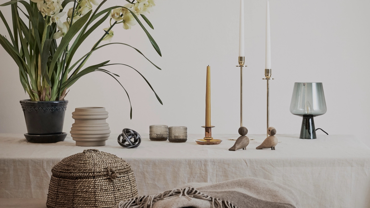 Innredning, lysestaker, lyslykter, vaser og ligende på bord med beige linduk