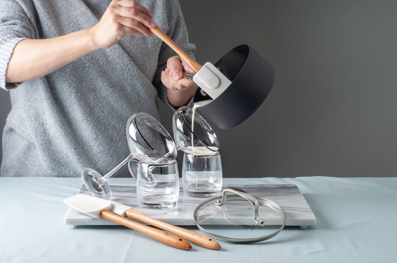 Vaaleanpunainen kulho ja nuolija muumikuviolla ovat pöydällä kukkien vieressä.