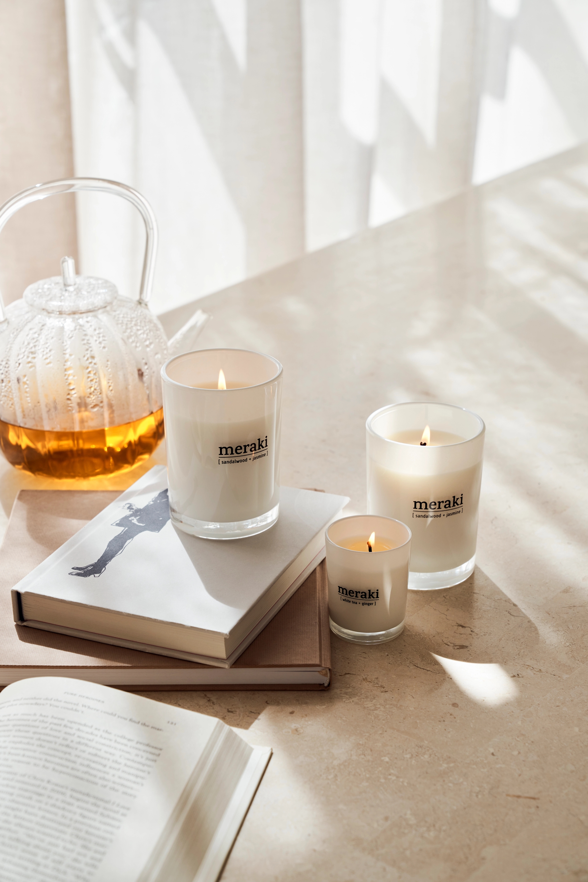 Tre lys fra Meraki står på et bord ved siden av en bok