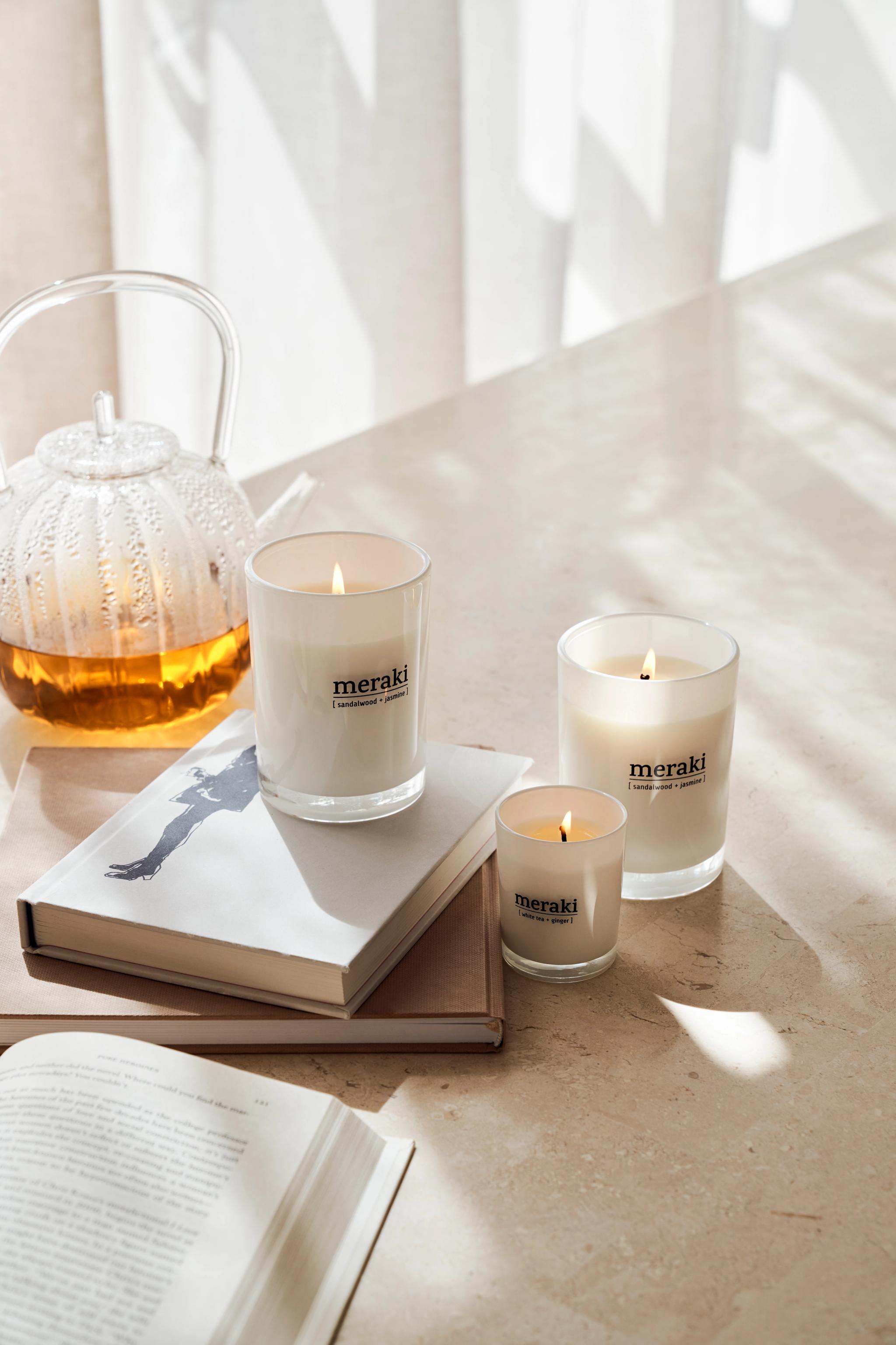 Tre lys fra Meraki står på et bord ved siden av en bok