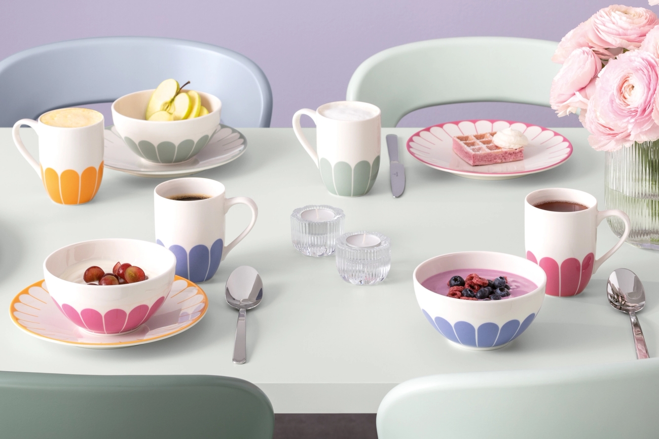 Fargerik frokostborddekking med mønstret servise, kaffe, yoghurt og frukt i pastellfargede omgivelser.