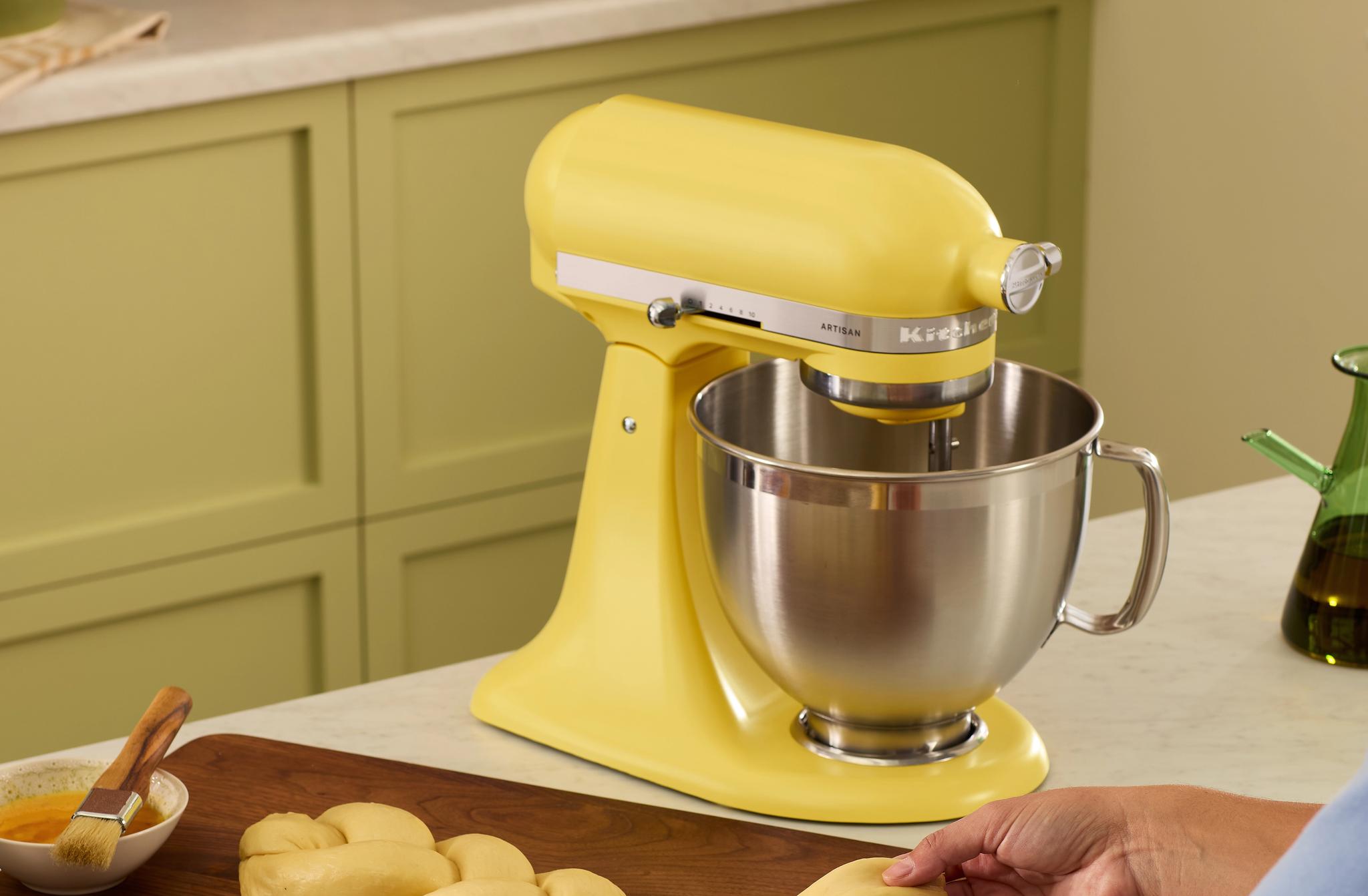 Keltainen KitchenAid-yleiskone ja käsin letitettävä taikina keittiön työtasolla.