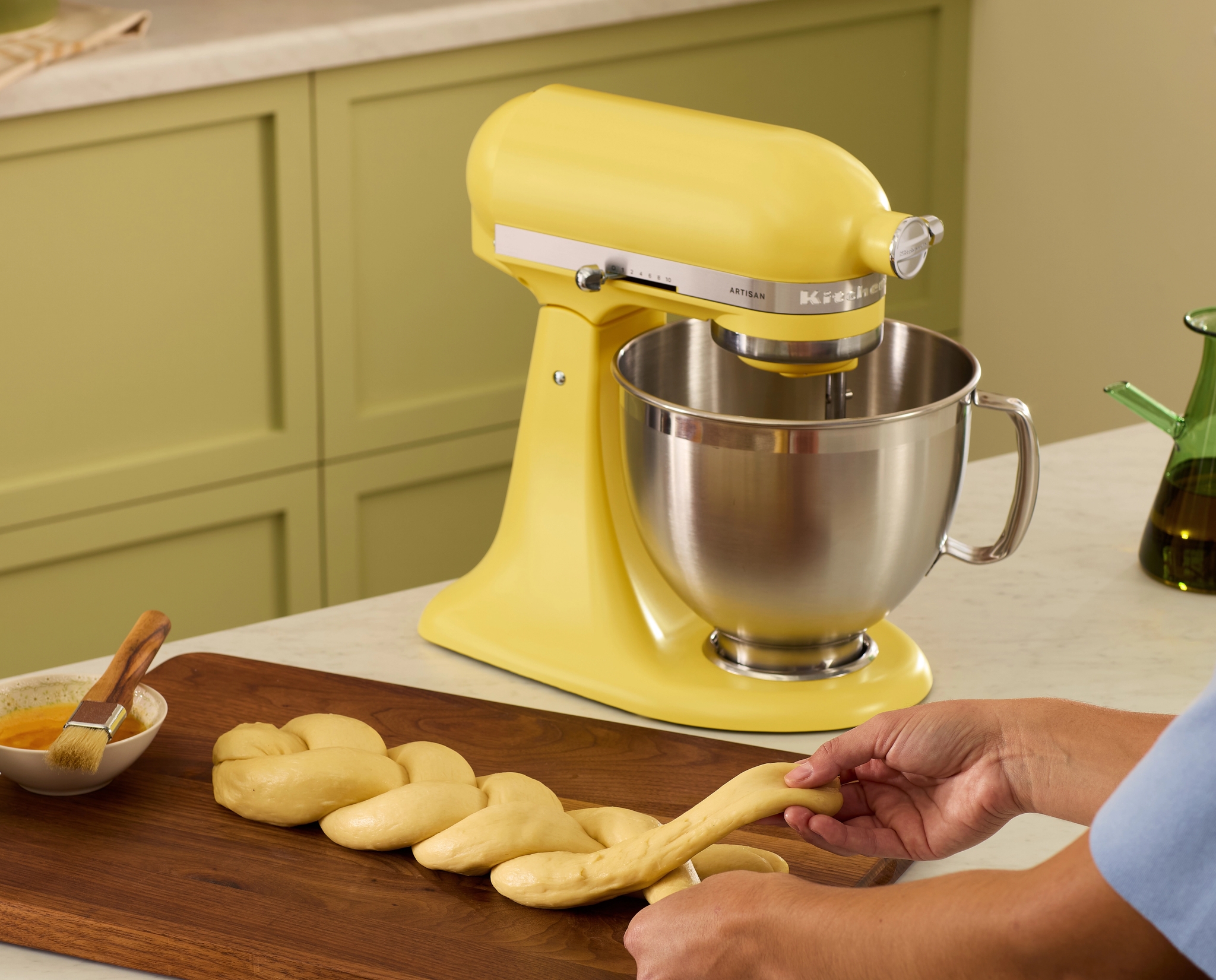 Keltainen KitchenAid-yleiskone ja käsin letitettävä taikina keittiön työtasolla.