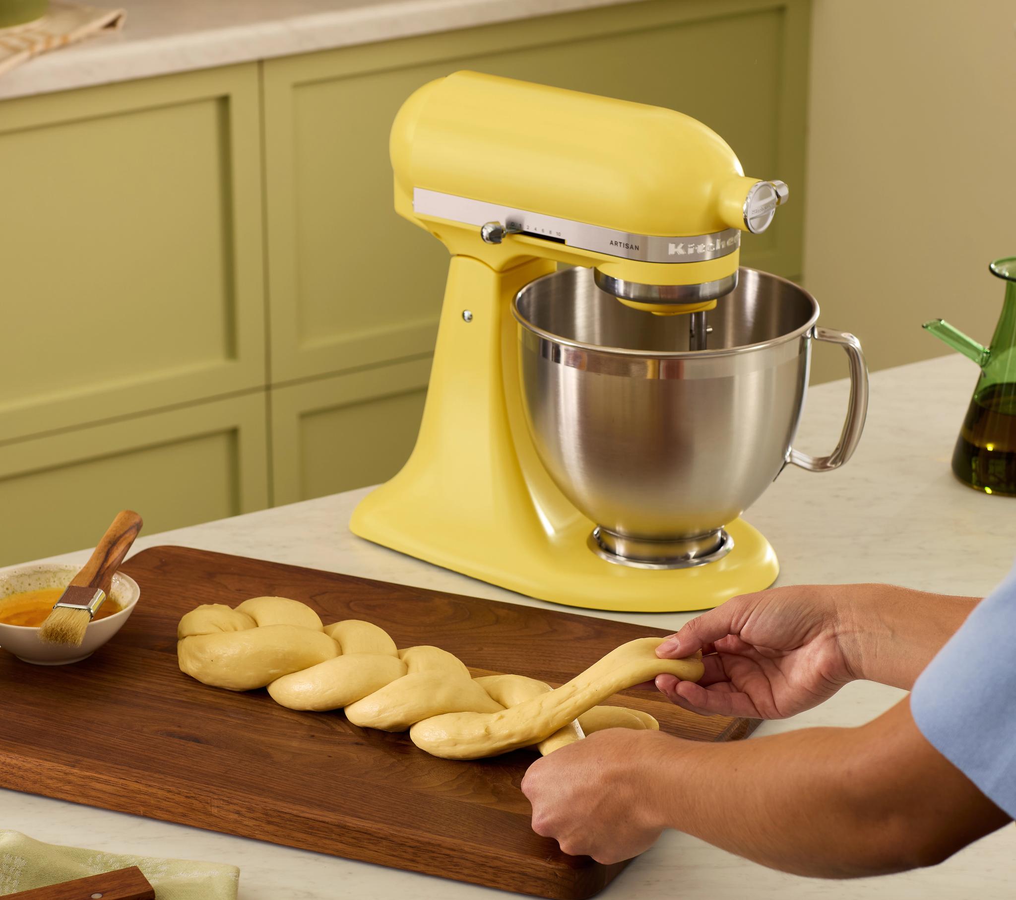 Keltainen KitchenAid-yleiskone ja käsin letitettävä taikina keittiön työtasolla.