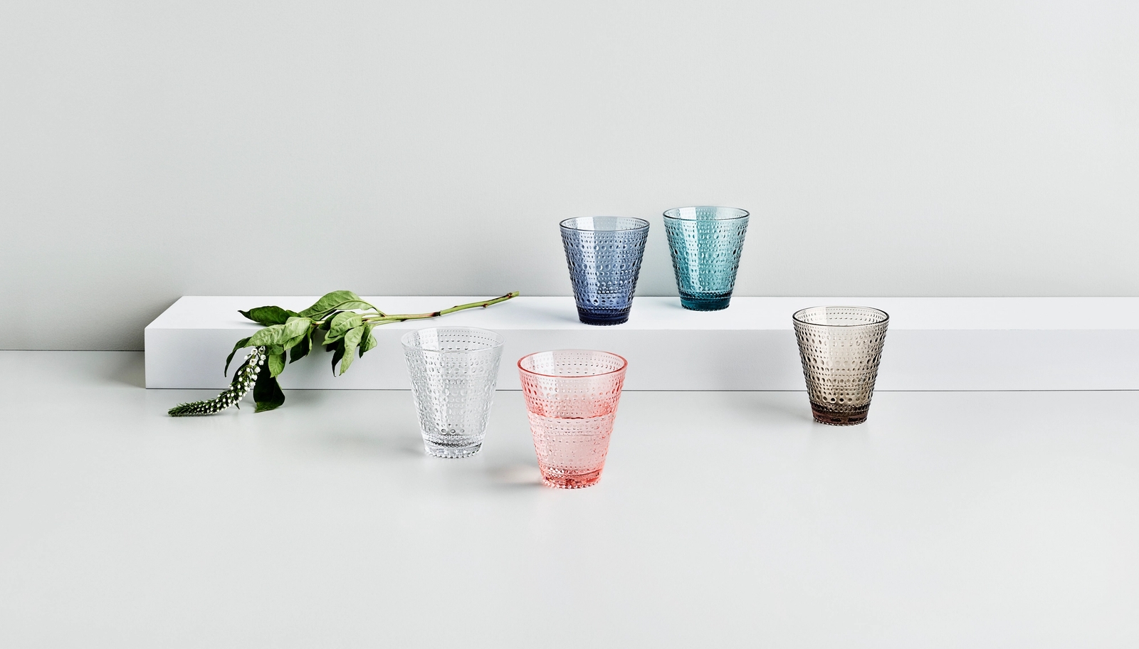 Dricksglas Iittala kastehelmi i olika färger samt grön kvist mot vit bakgrund