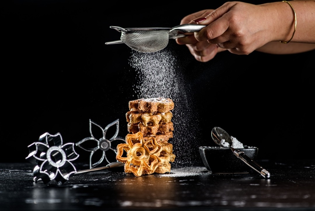 a person is dusting a stack of waffles with powdered sugar .
