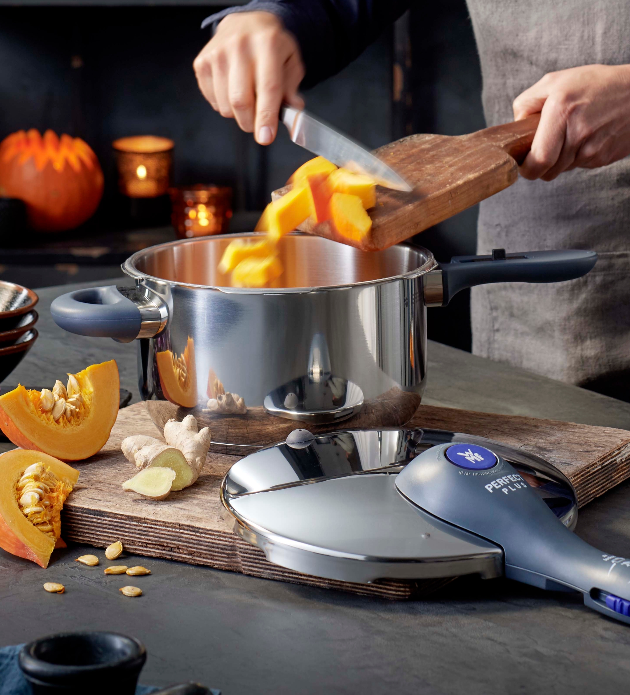 Lähikuva kokin käsivarresta puisella keittiön tasolla vasaroitujen ruostumattomasta teräksestä valmistettujen keittoastioiden vieressä.