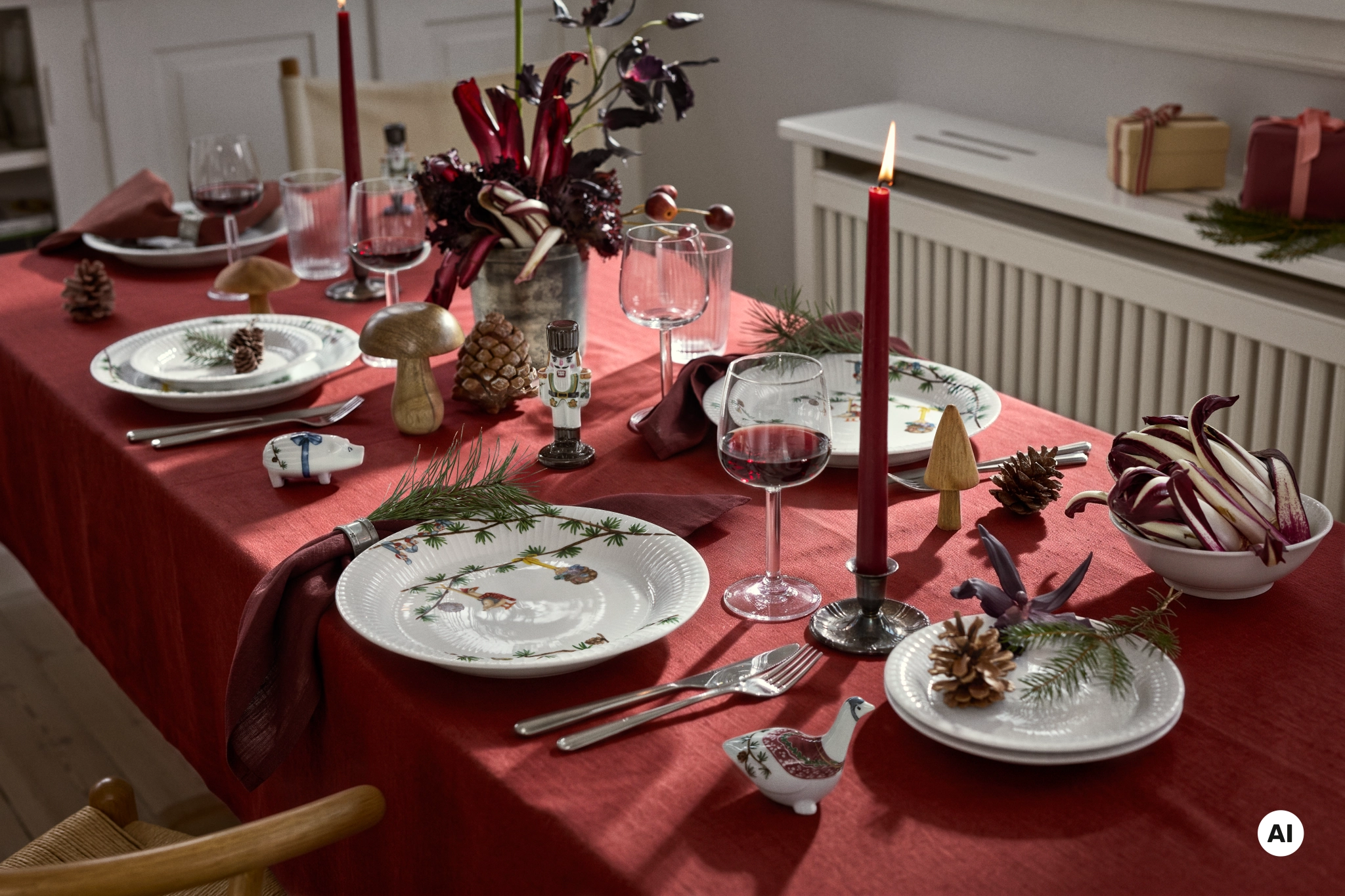 Juldukning med röd duk, tända ljus, julporslin, kottar, grankvistar och dekorativa figurer.