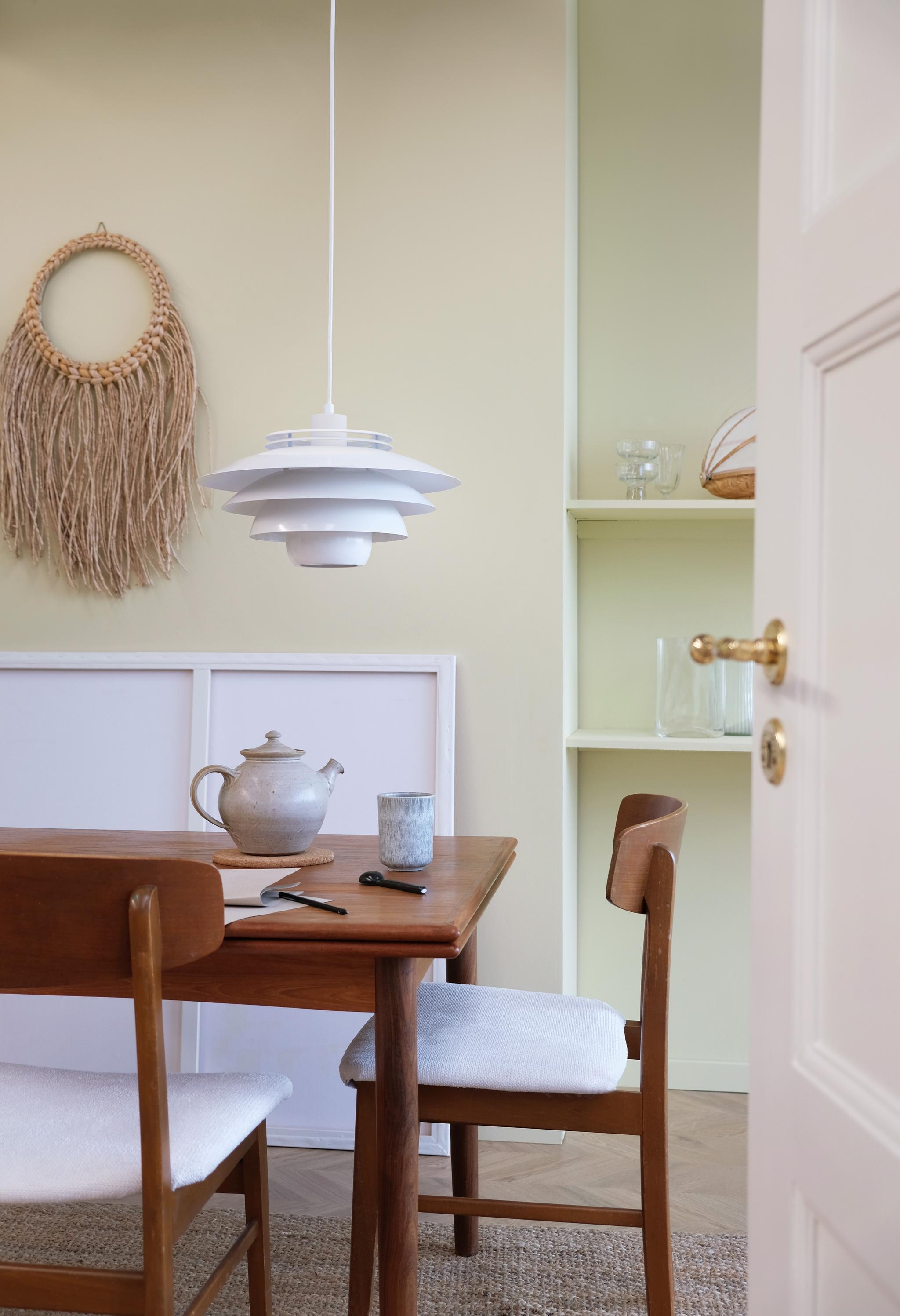 matplats med ett brunt träbord och stolar omgiven av rosa vägg med en vit taklampa ovanför