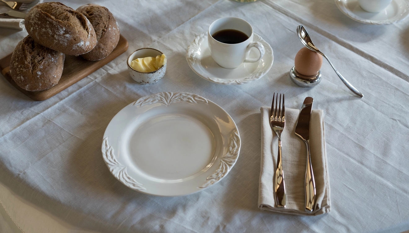 et dekket bord til frokost med tallerkener, kopper, bestikk og brød.