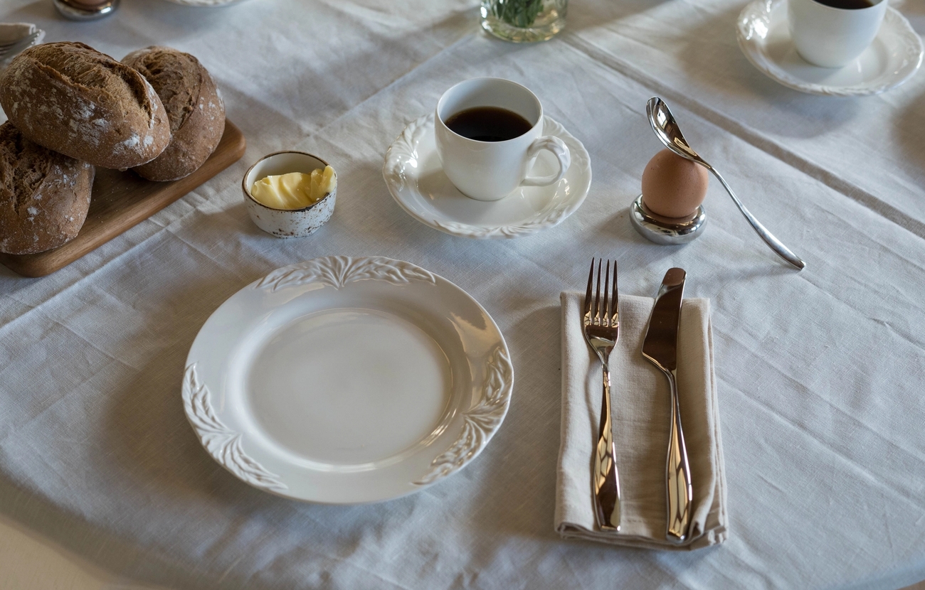 ett dukat bord för frukost med tallrikar, koppar, bestick och bröd.