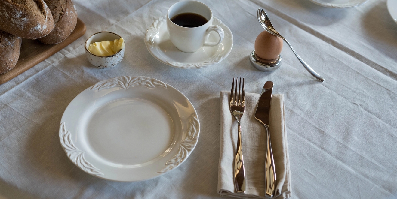 ett dukat bord för frukost med tallrikar, koppar, bestick och bröd.